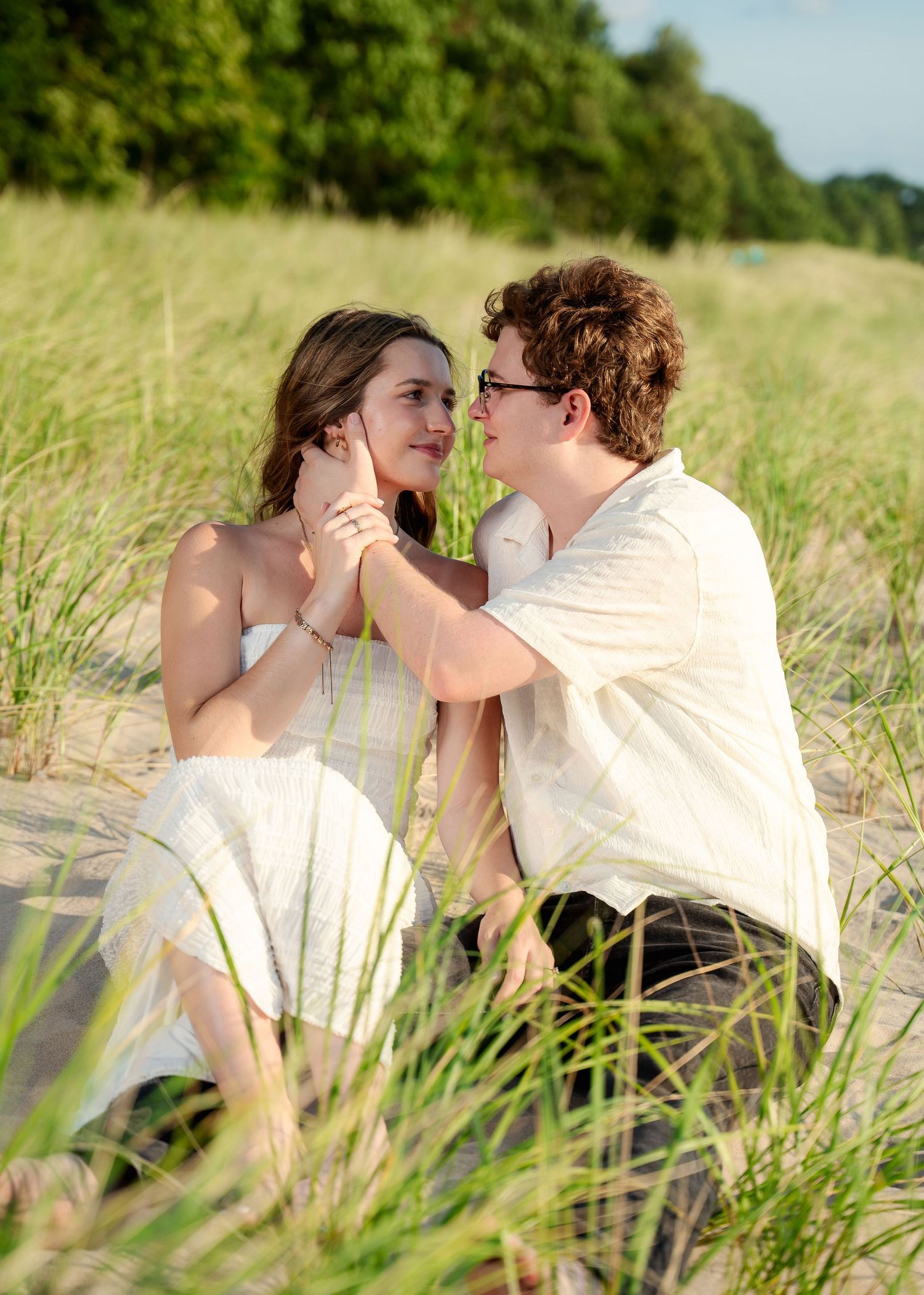 Couple sharing an intimate moment while sitting in tall grass on a sunny summer day.