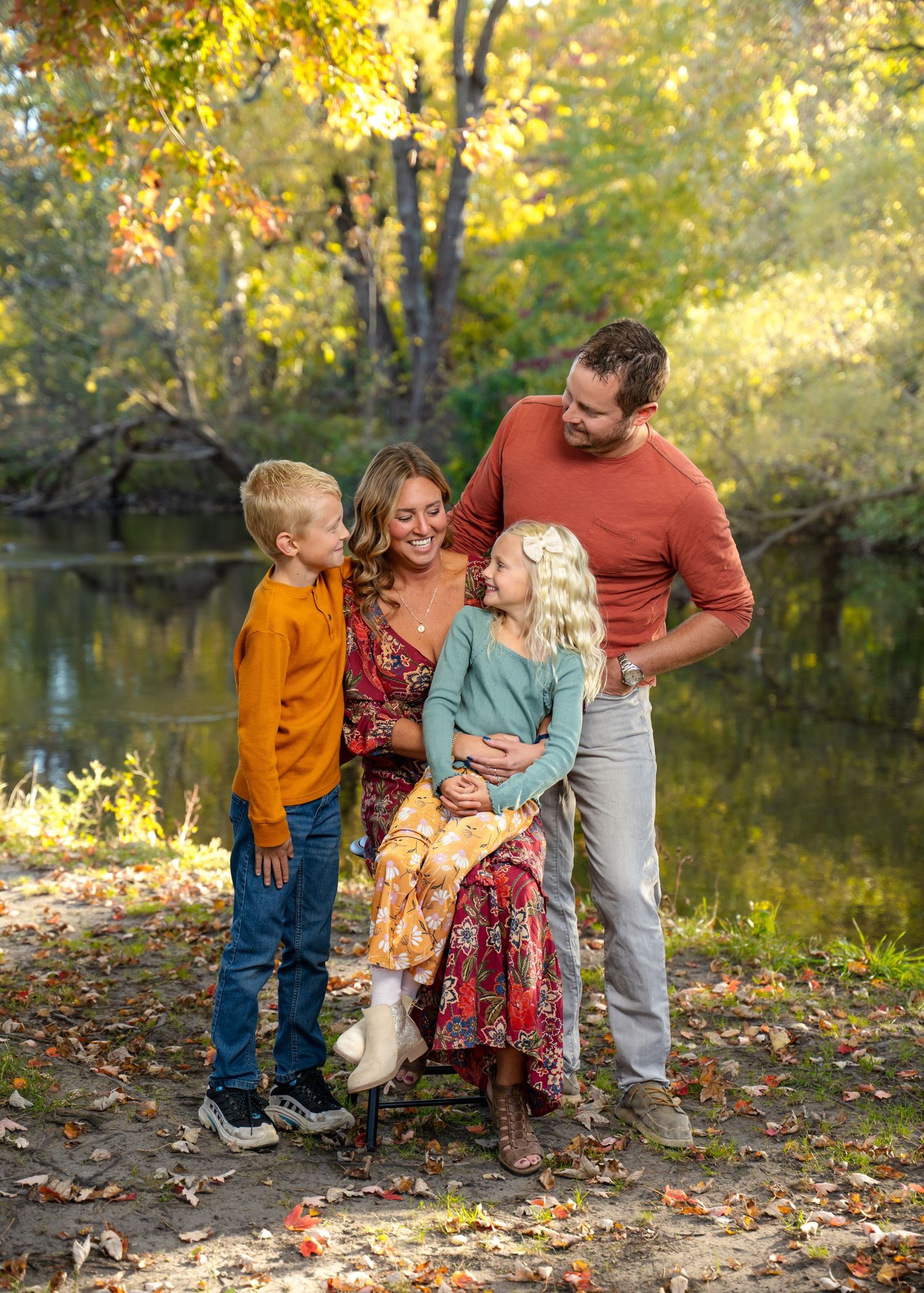 Candid family moment by riverside with fall foliage and warm sunlight.