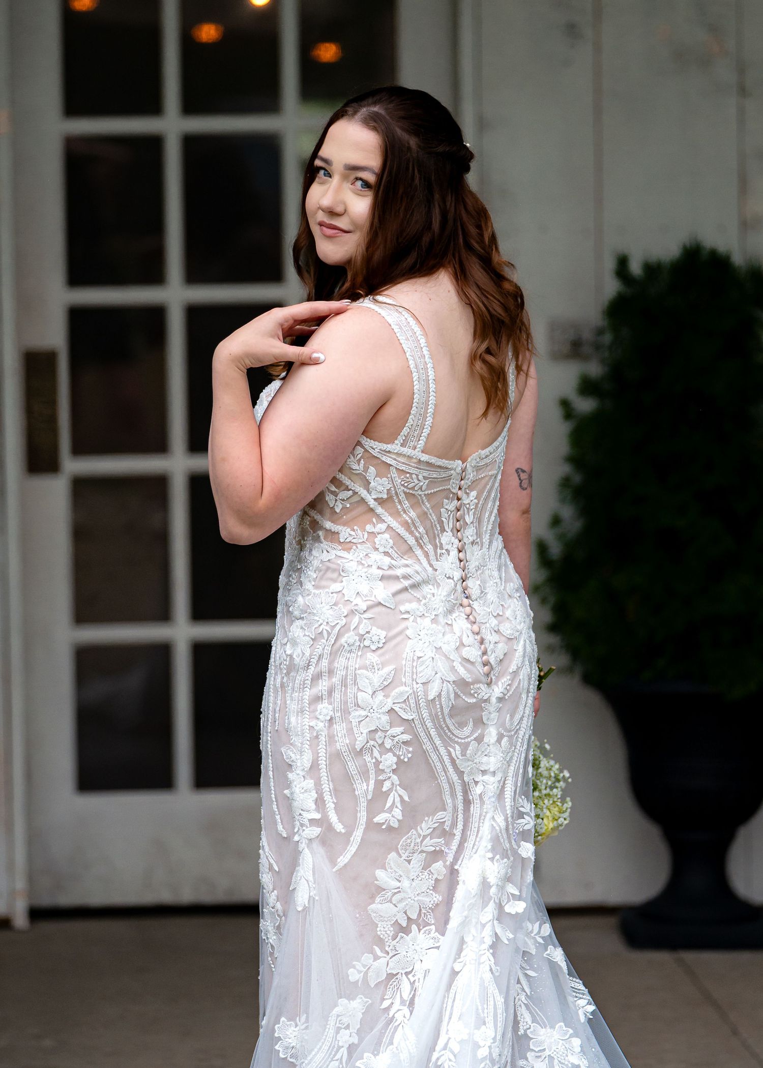 Bride in elegant lace mermaid wedding gown posing outdoors, showcasing intricate floral embroidery and corset back.