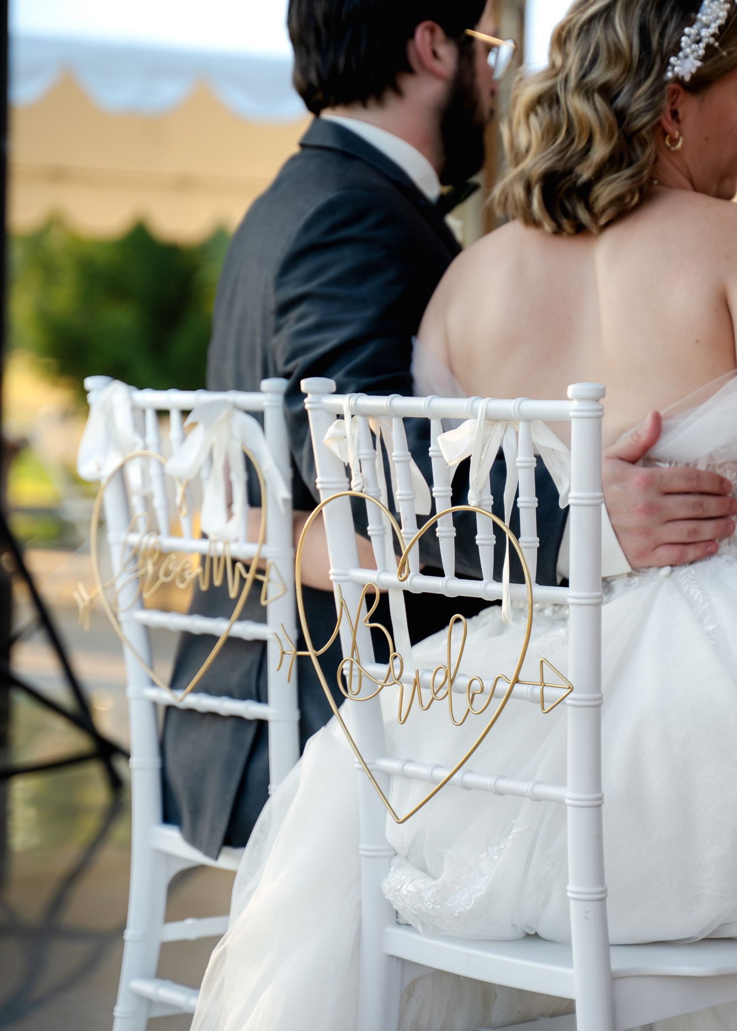 White wedding chairs with decorative signs arranged in a row at an outdoor ceremony.