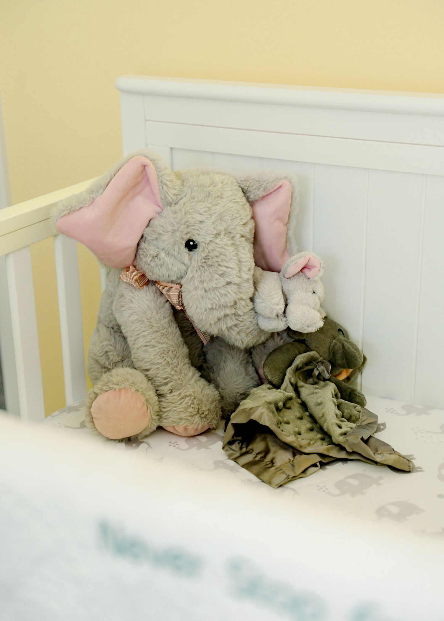 Stuffed elephant toys arranged on white bedding in a nursery setting.