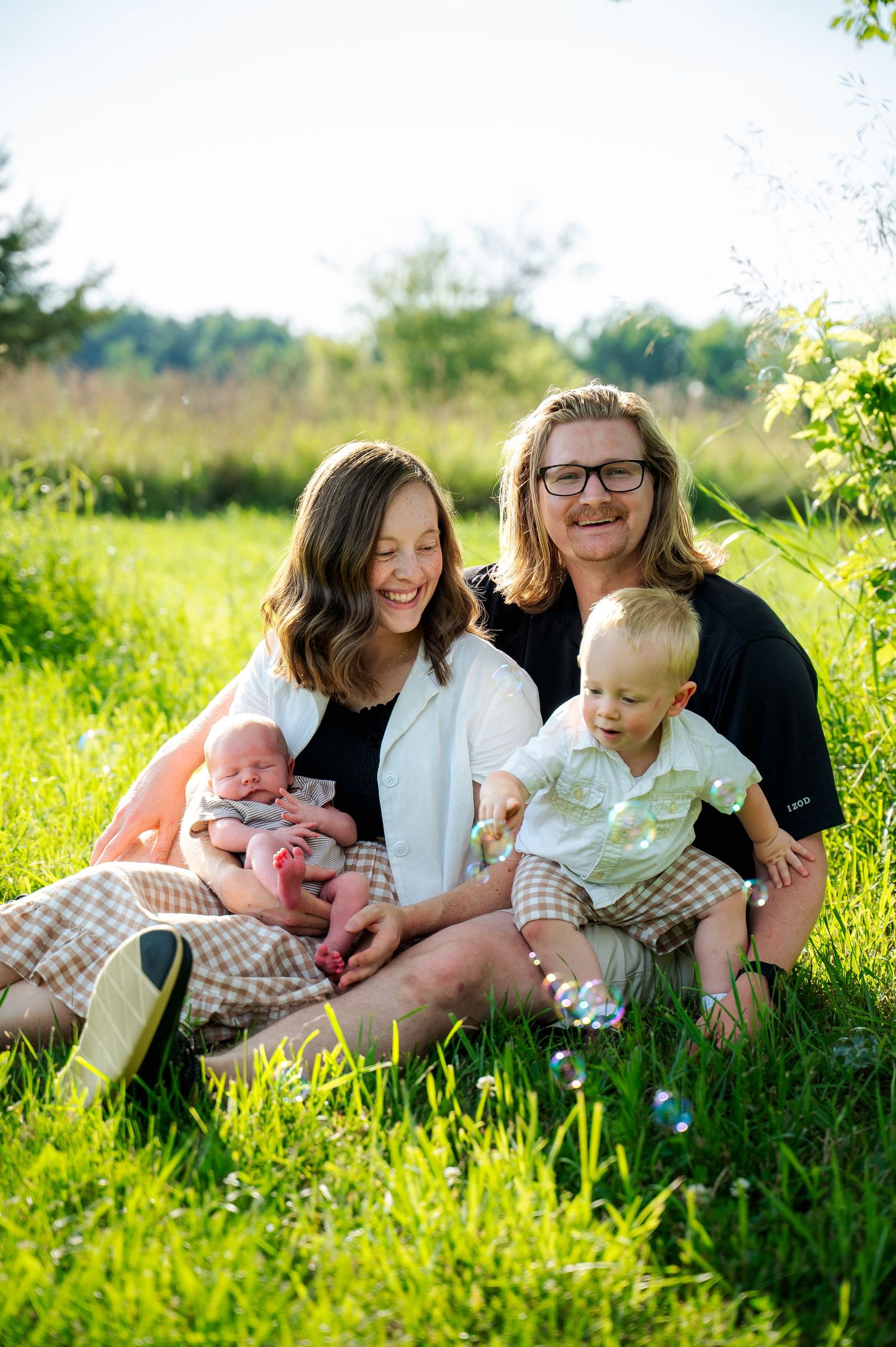 Family relaxing together on grass during an outdoor photo session in golden sunlight.