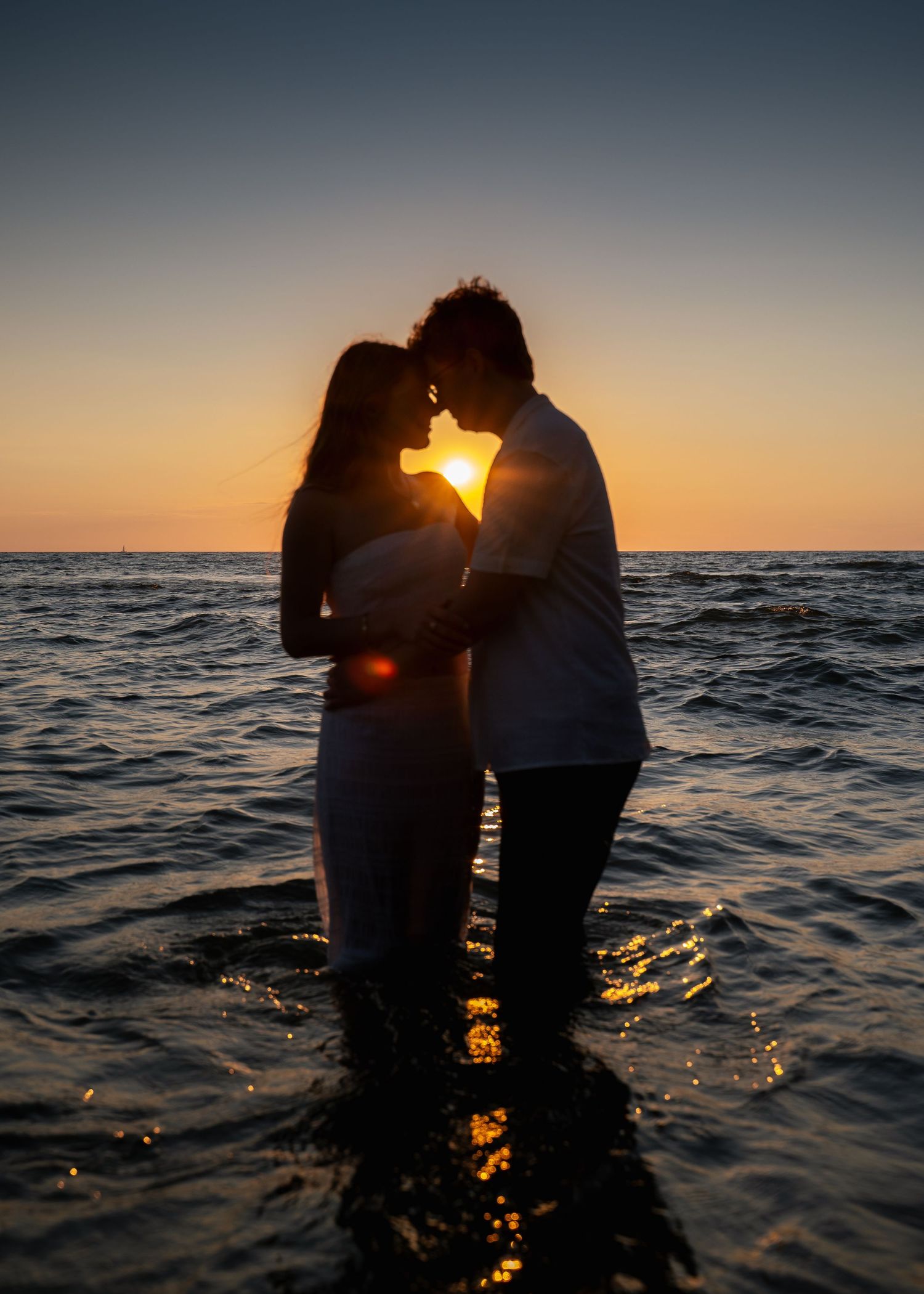 Silhouetted couple embracing in ocean water during golden sunset.