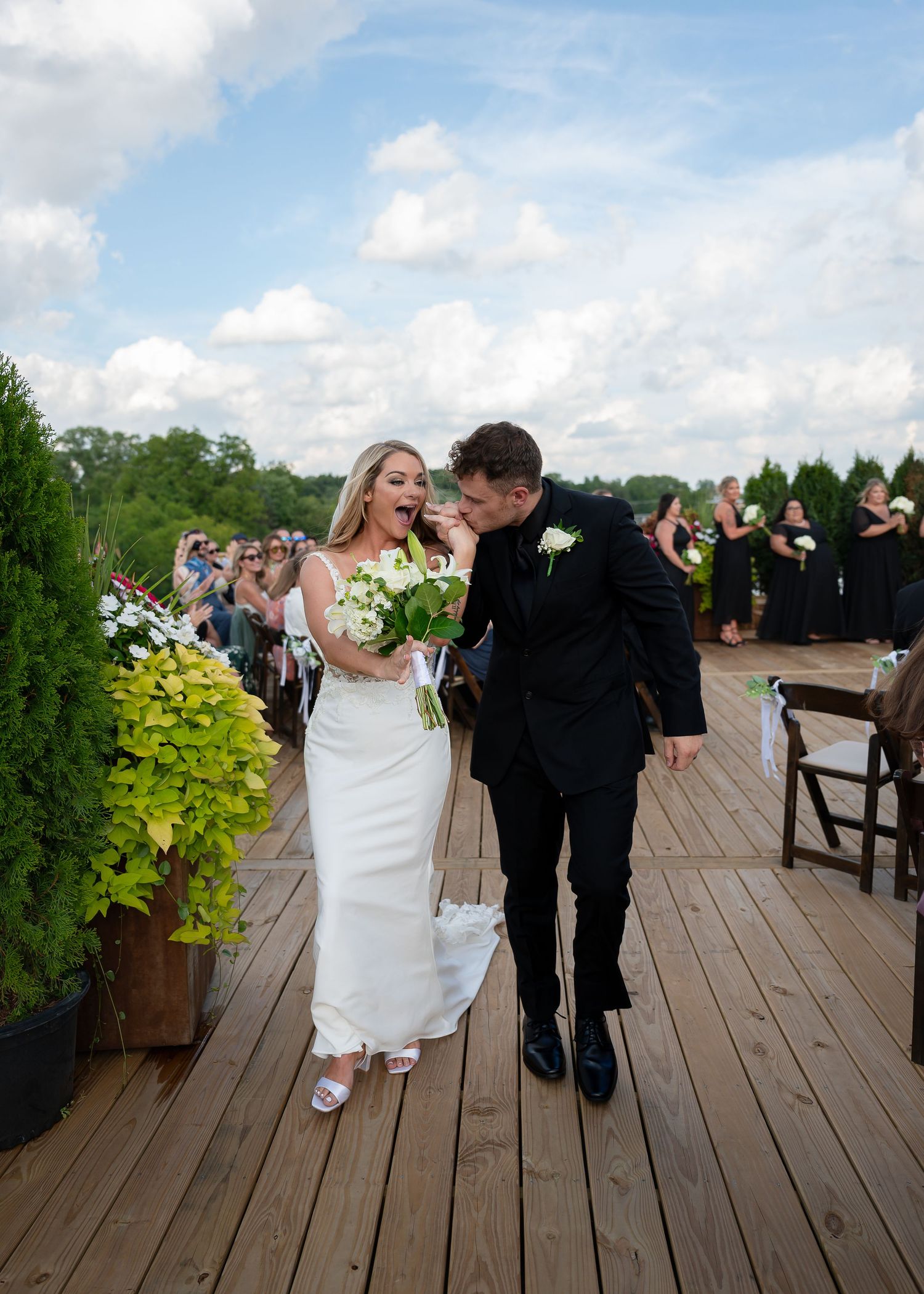 Bride and groom laughing joyfully as they walk back down the aisle after their outdoor wedding ceremony on a wooden deck.