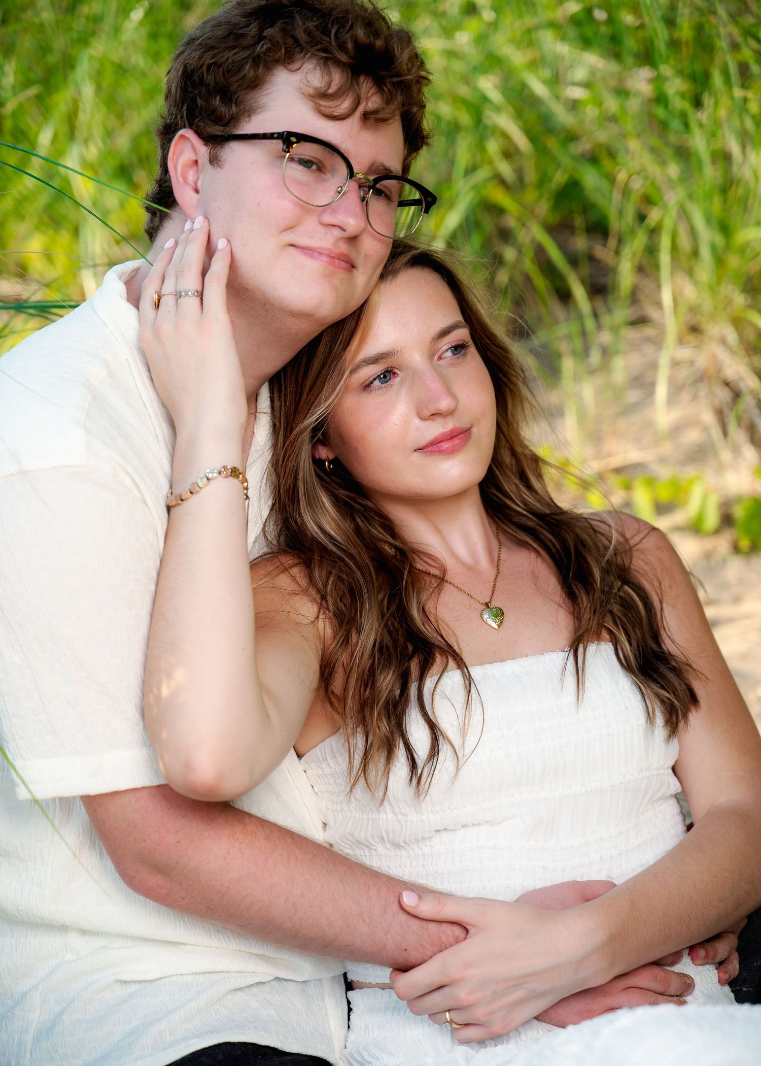 Couple in white clothing pose together against natural backdrop of tall grass.