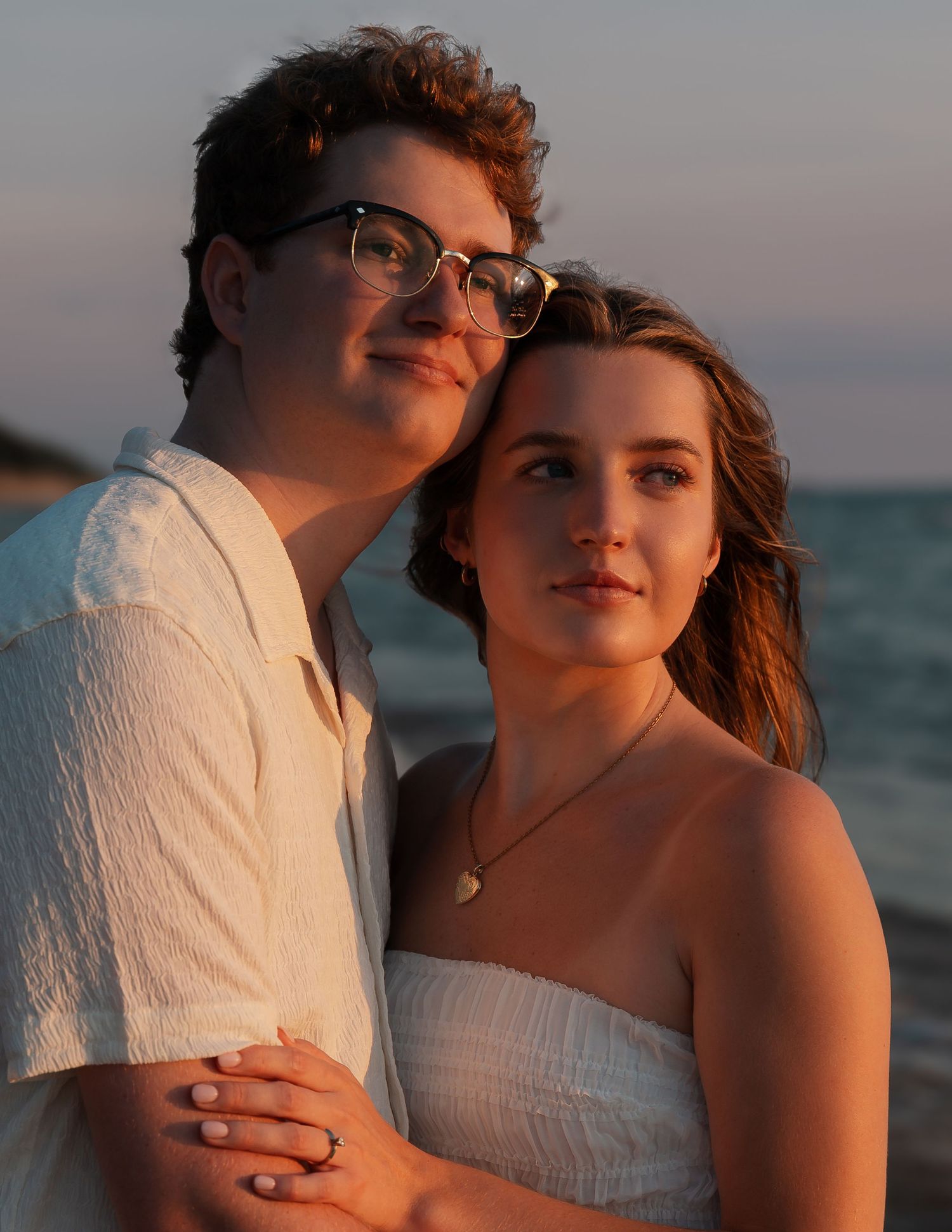 A romantic beach photoshoot at sunset captures tender moments between a couple in white attire.