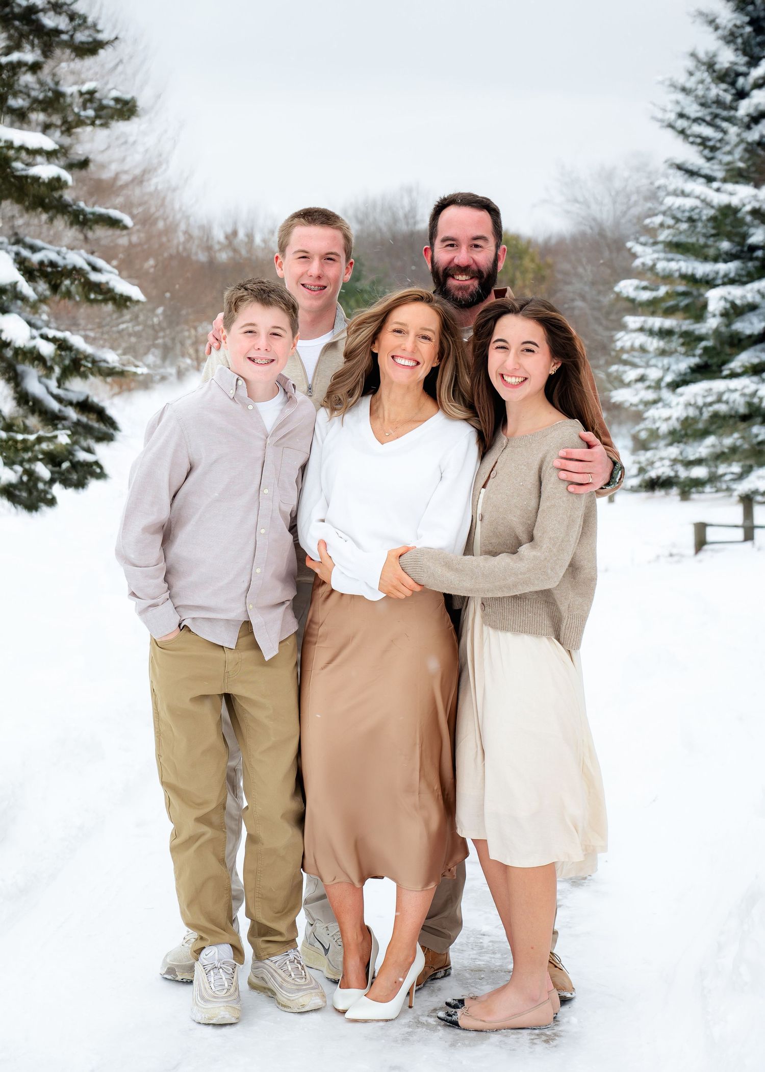 Winter family portrait outdoors with snow-covered evergreen trees in the background.