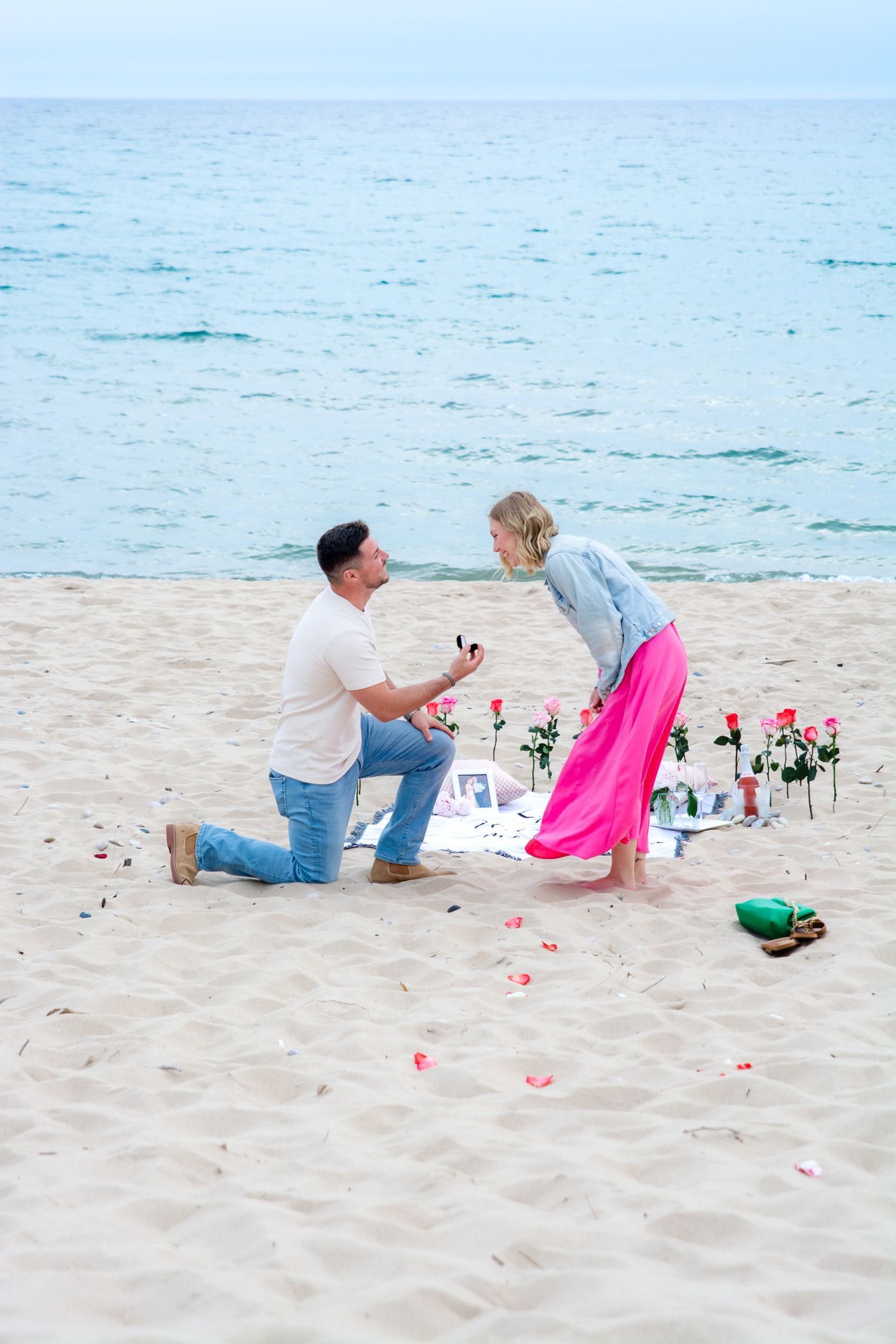 Beach proposal scene with rose petals and decorations on sandy shoreline.