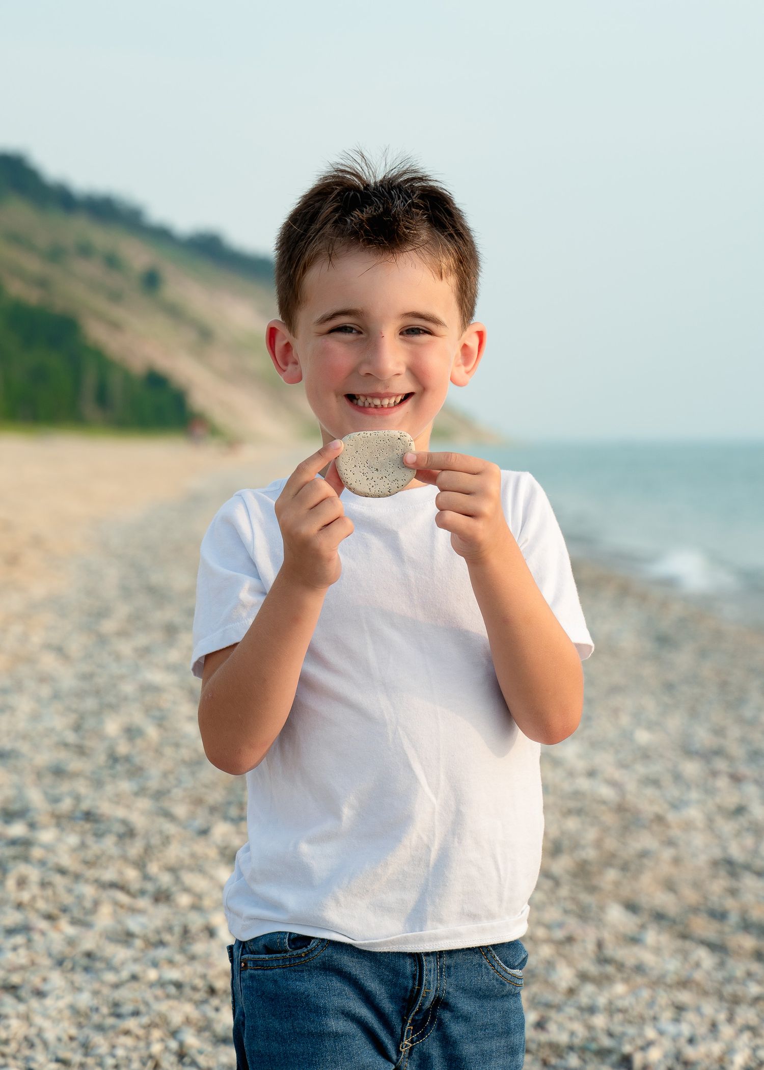 Child playing and smiling on rocky beach with ocean and cliffs in background.