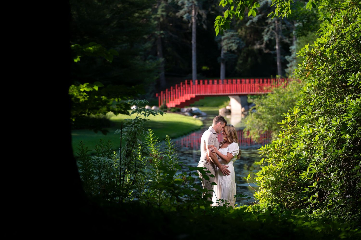 Couple embracing in a lush garden with a red bridge backdrop, perfect for romantic wedding photography.