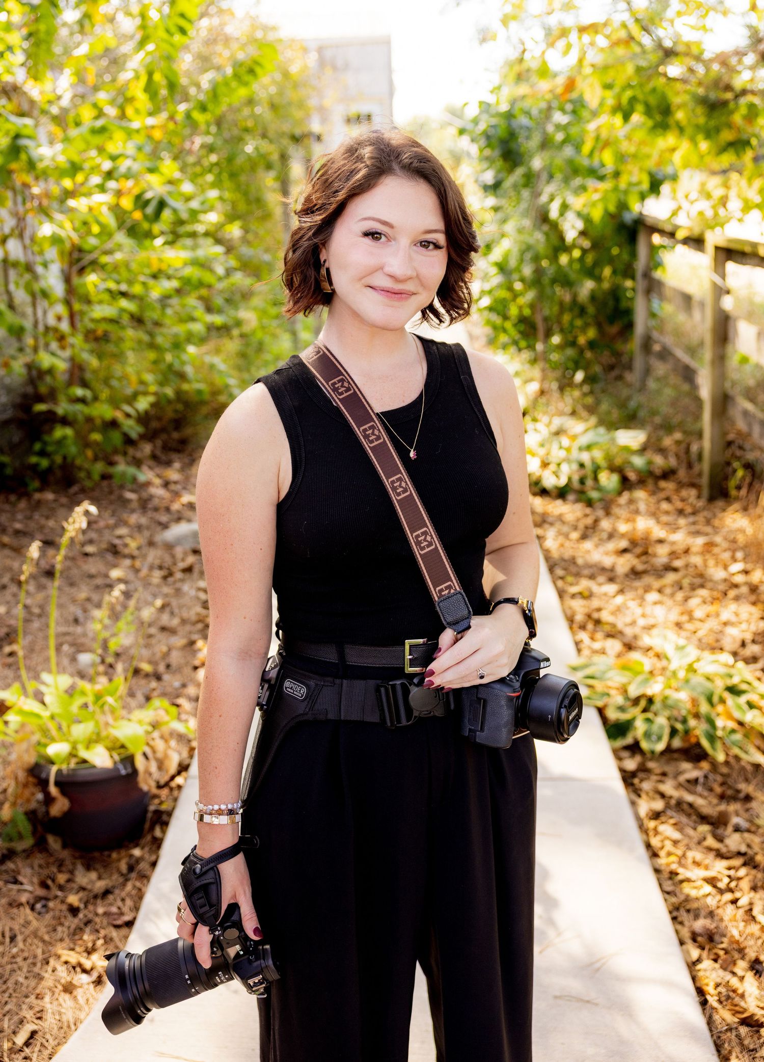 Professional photographer in black dress with dual camera setup posing outdoors.