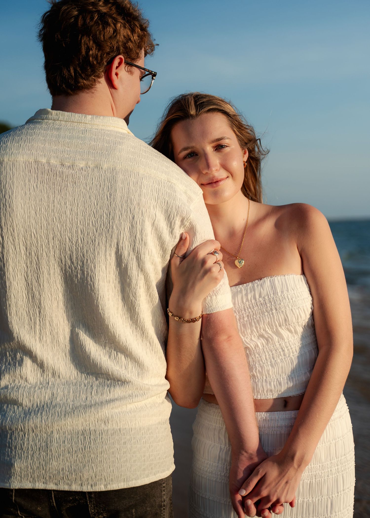 Couple in white outfits sharing tender moment on beach.