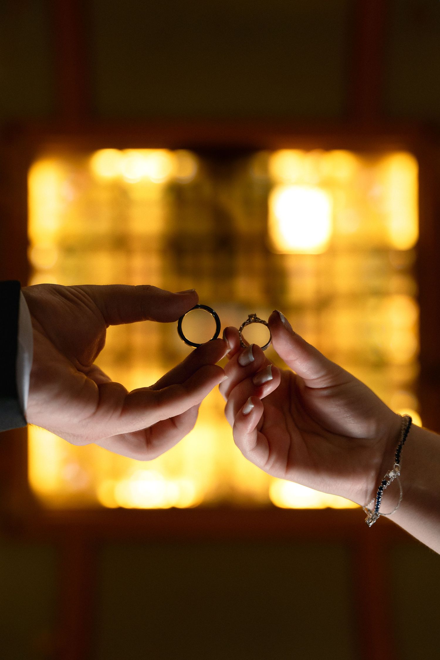 Two hands holding wedding rings against a warm golden glowing background, symbolizing love and commitment.