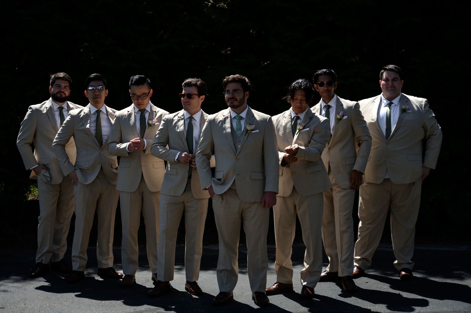 Group of eight groomsmen in matching tan suits posing outdoors for a wedding party photo.