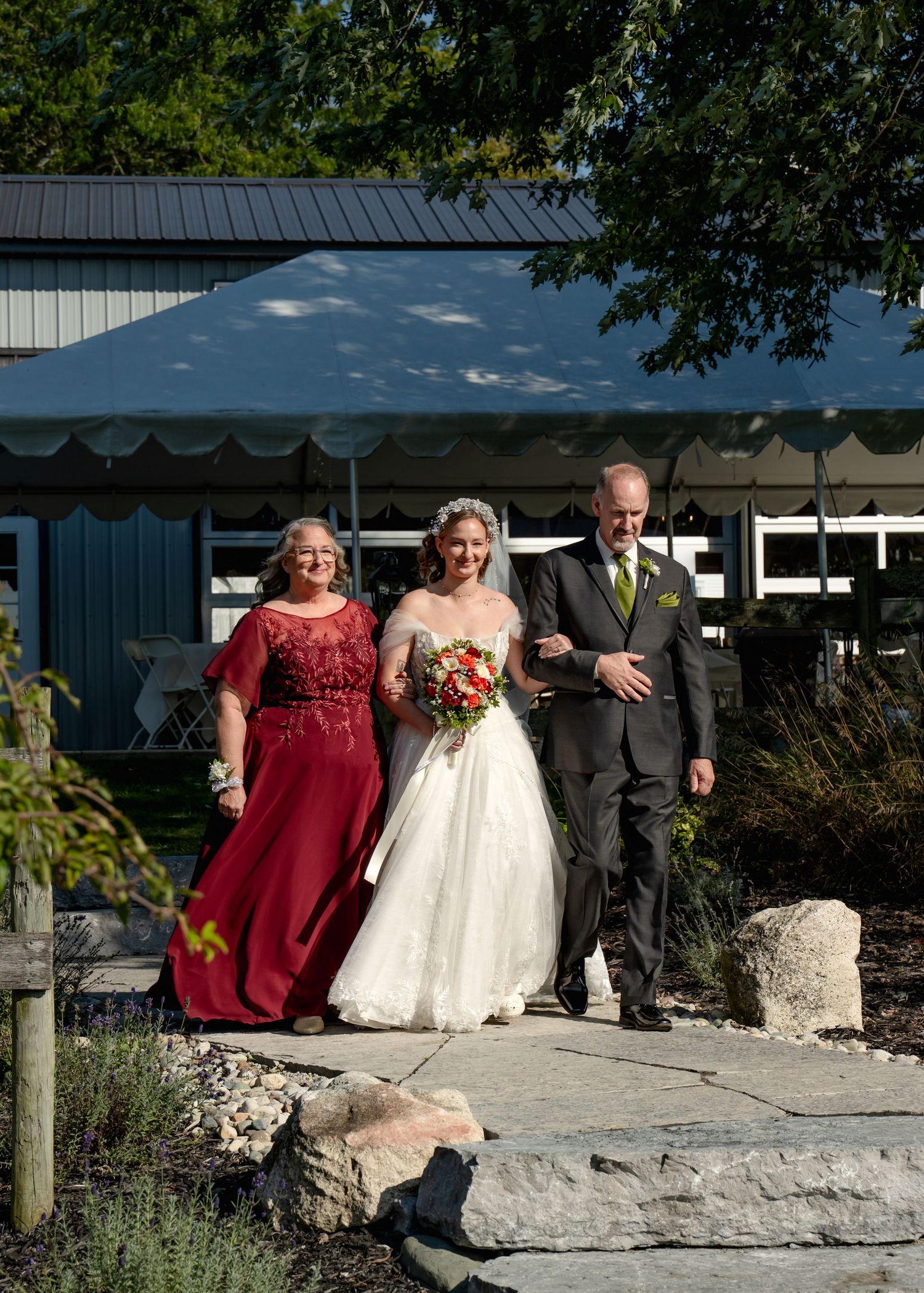 Wedding party walks together on stone path outside venue with bride in white gown and red accent dress.