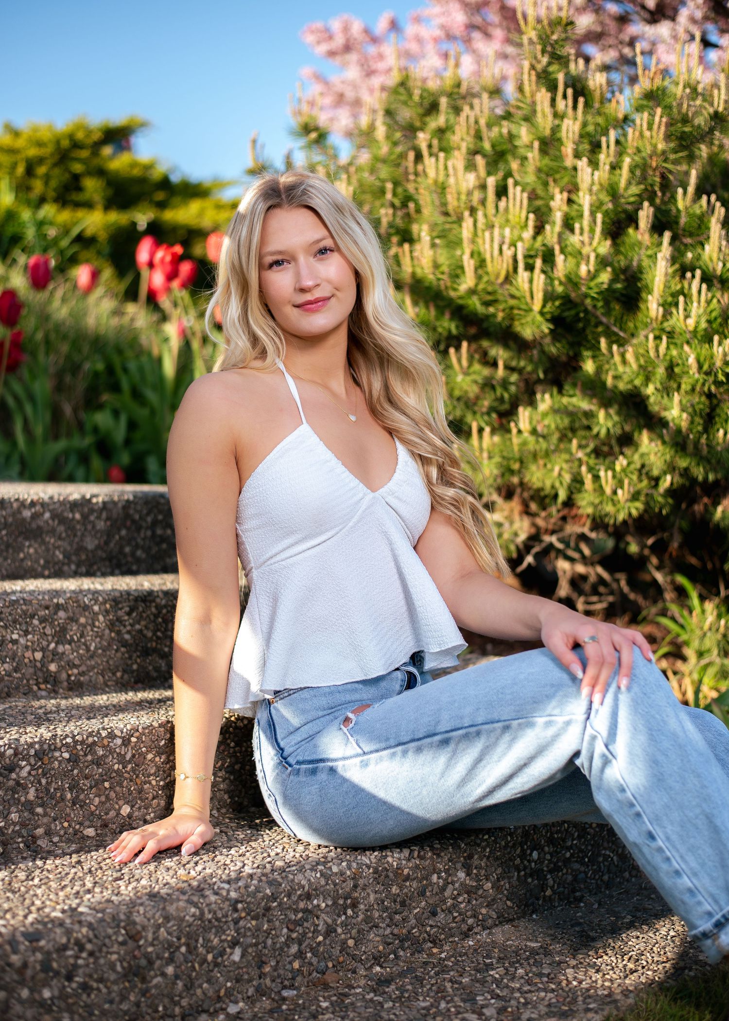 Casual summer portrait in white tank top and jeans on stone wall.
