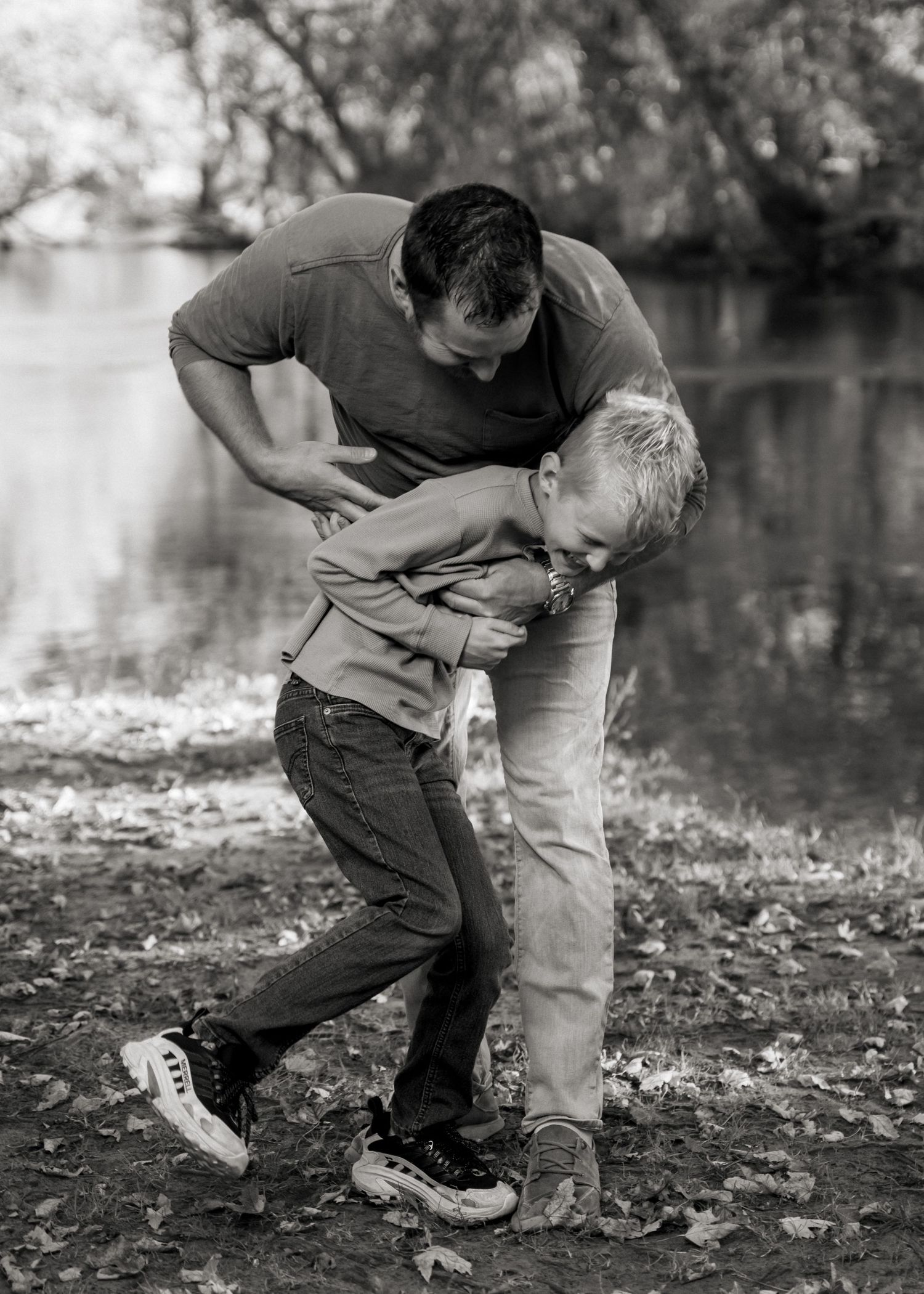 A playful black and white moment captured by a lake with fallen autumn leaves on the ground.
