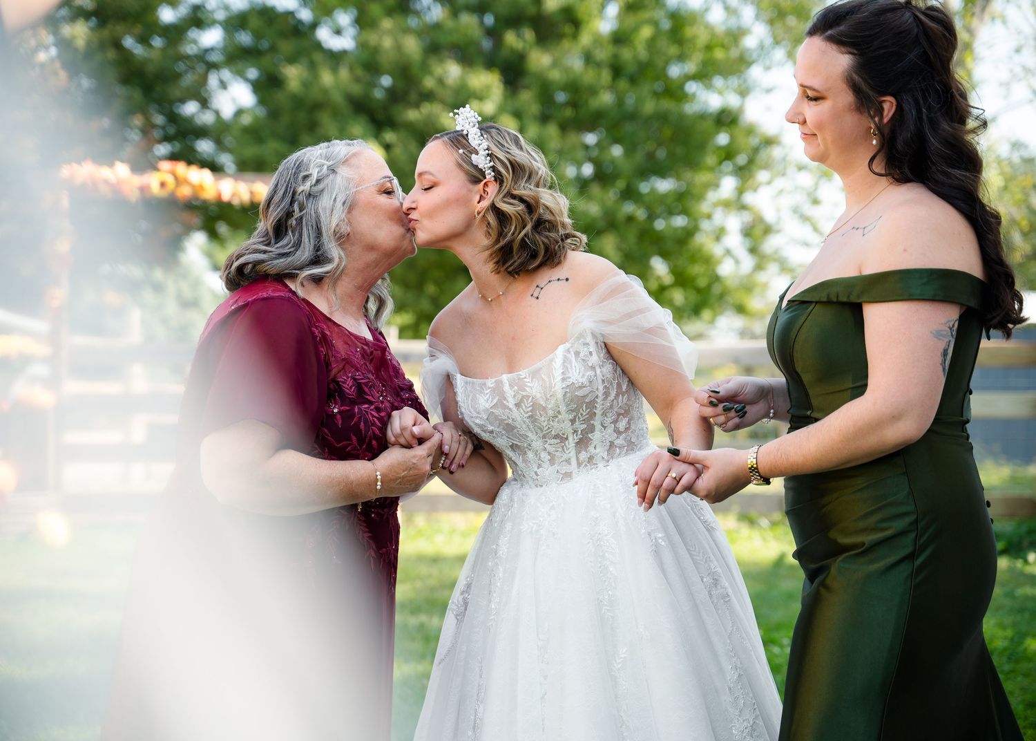 Bridal party members in burgundy and forest green dresses share candid moments during wedding photos.