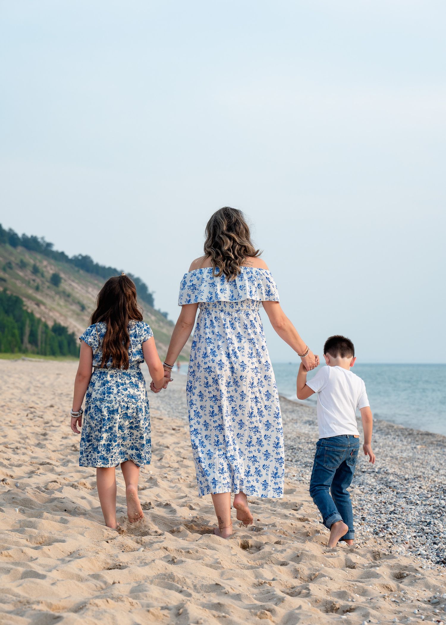 People walking hand in hand along a scenic beach with cliffs in the background.