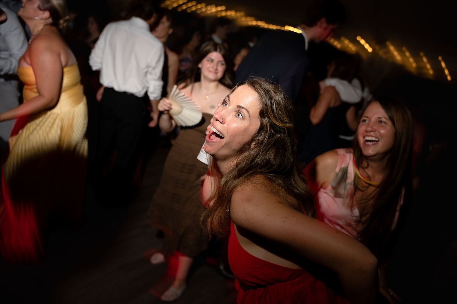 Women dancing and laughing at a lively party or wedding reception in elegant dresses.