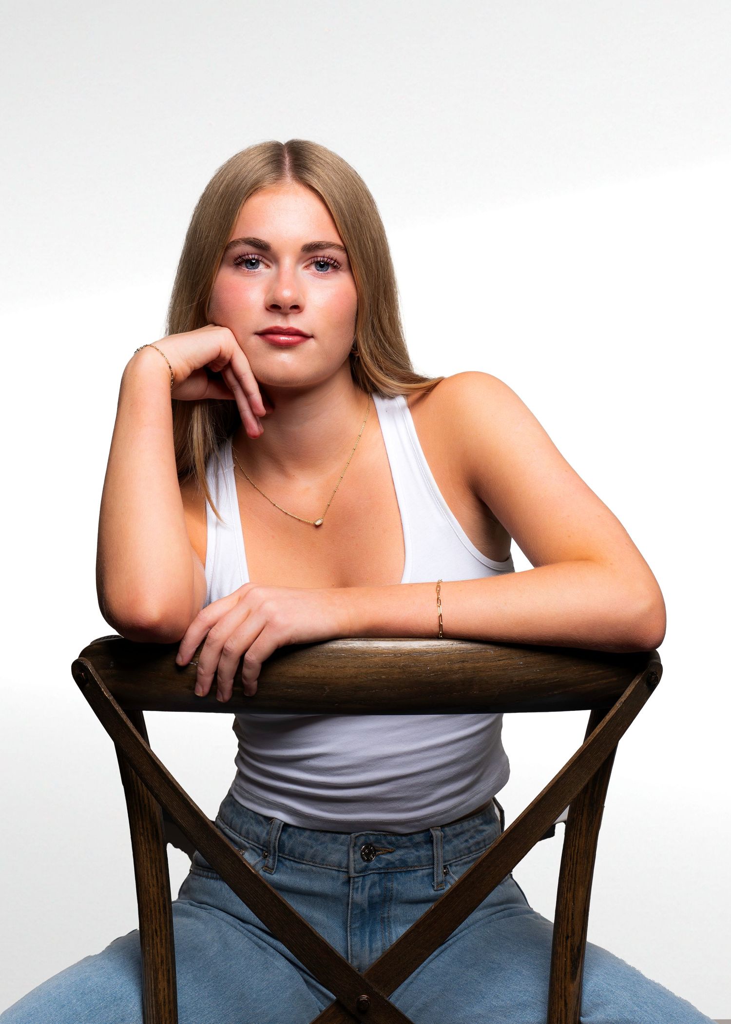 Studio portrait series showing poses in a white tank top and jeans while sitting on a wooden chair.