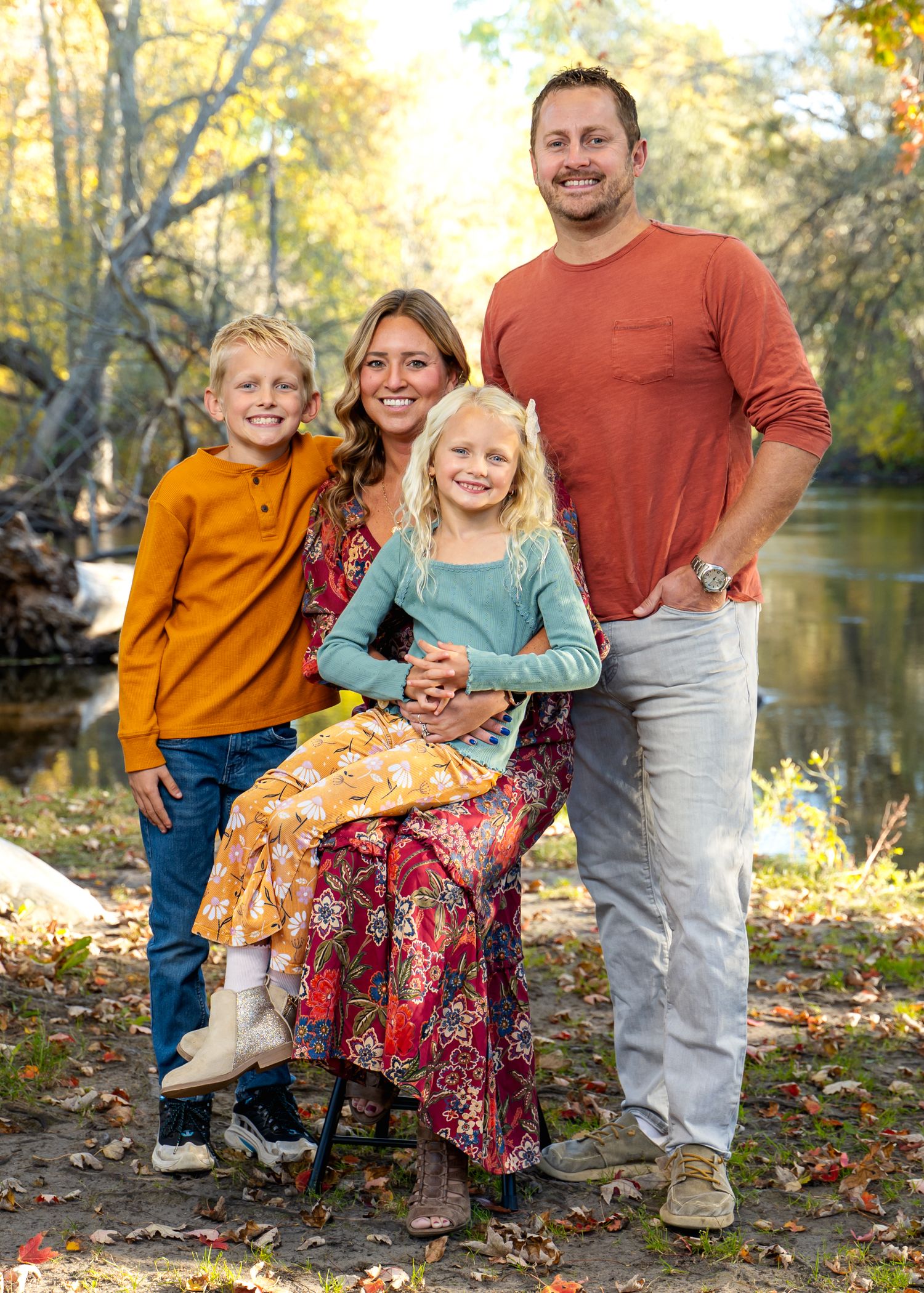 Family enjoying autumn day by riverside with fallen leaves and golden trees.