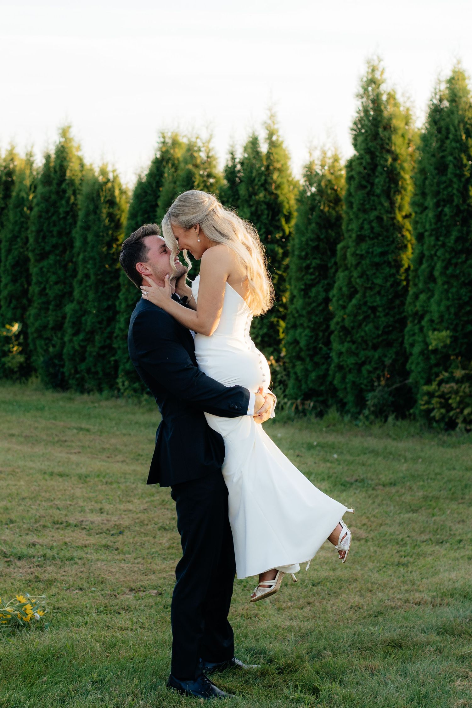 Groom lifts bride in romantic dance move during outdoor wedding photoshoot.