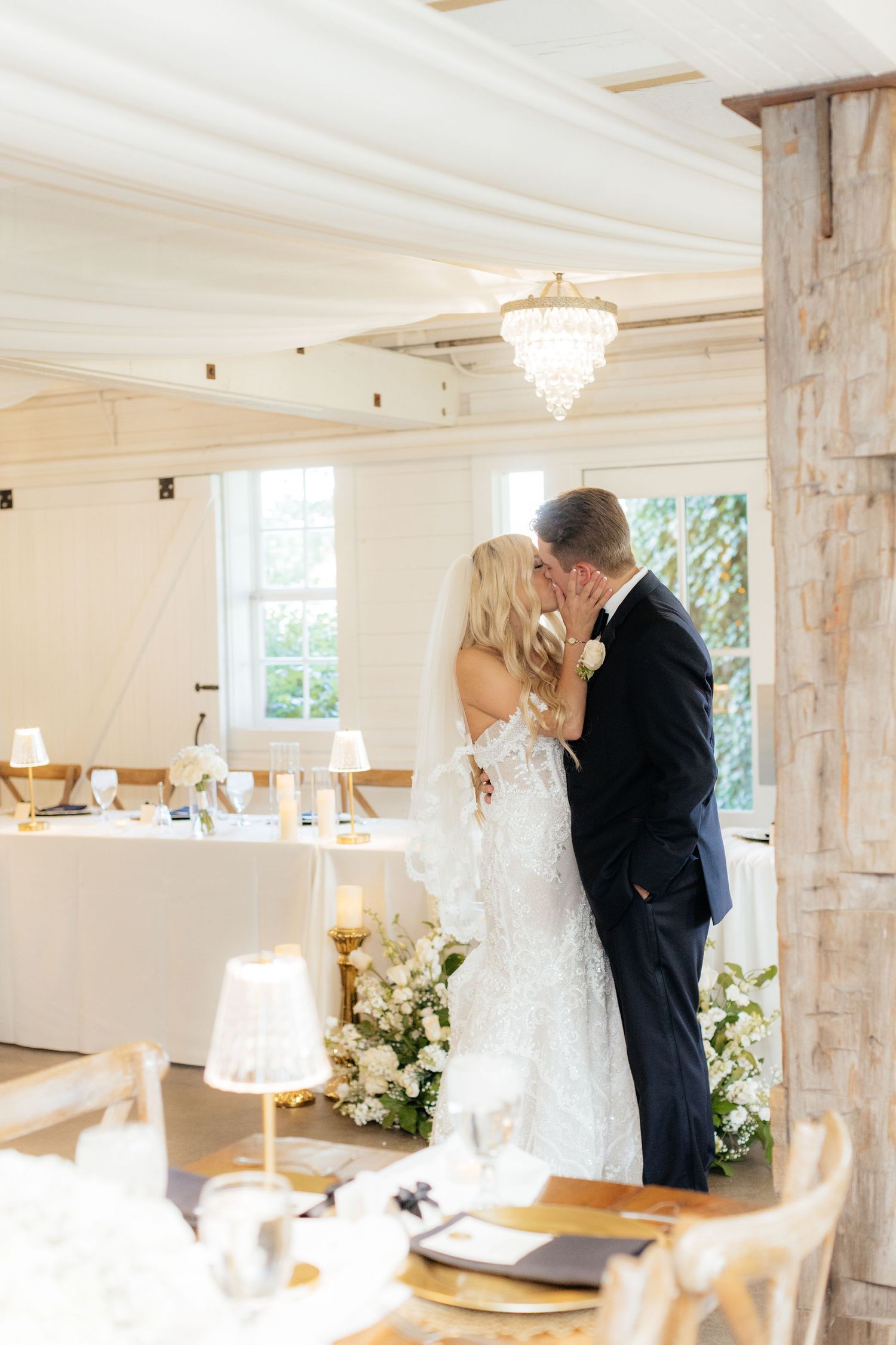 Wedding celebration in a bright white room with rustic wooden posts and chandeliers.