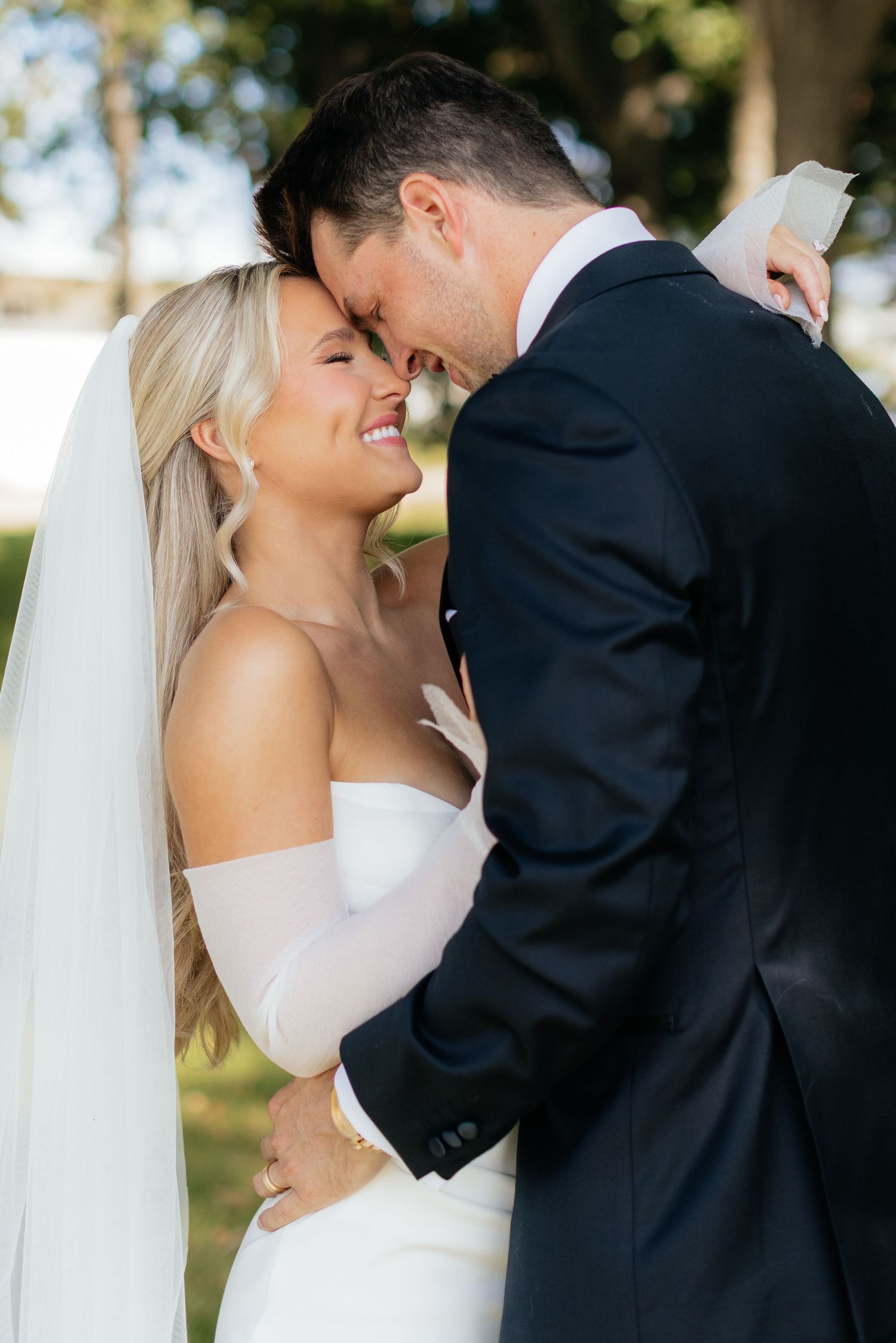 Newlyweds share tender moment in garden setting with natural lighting.