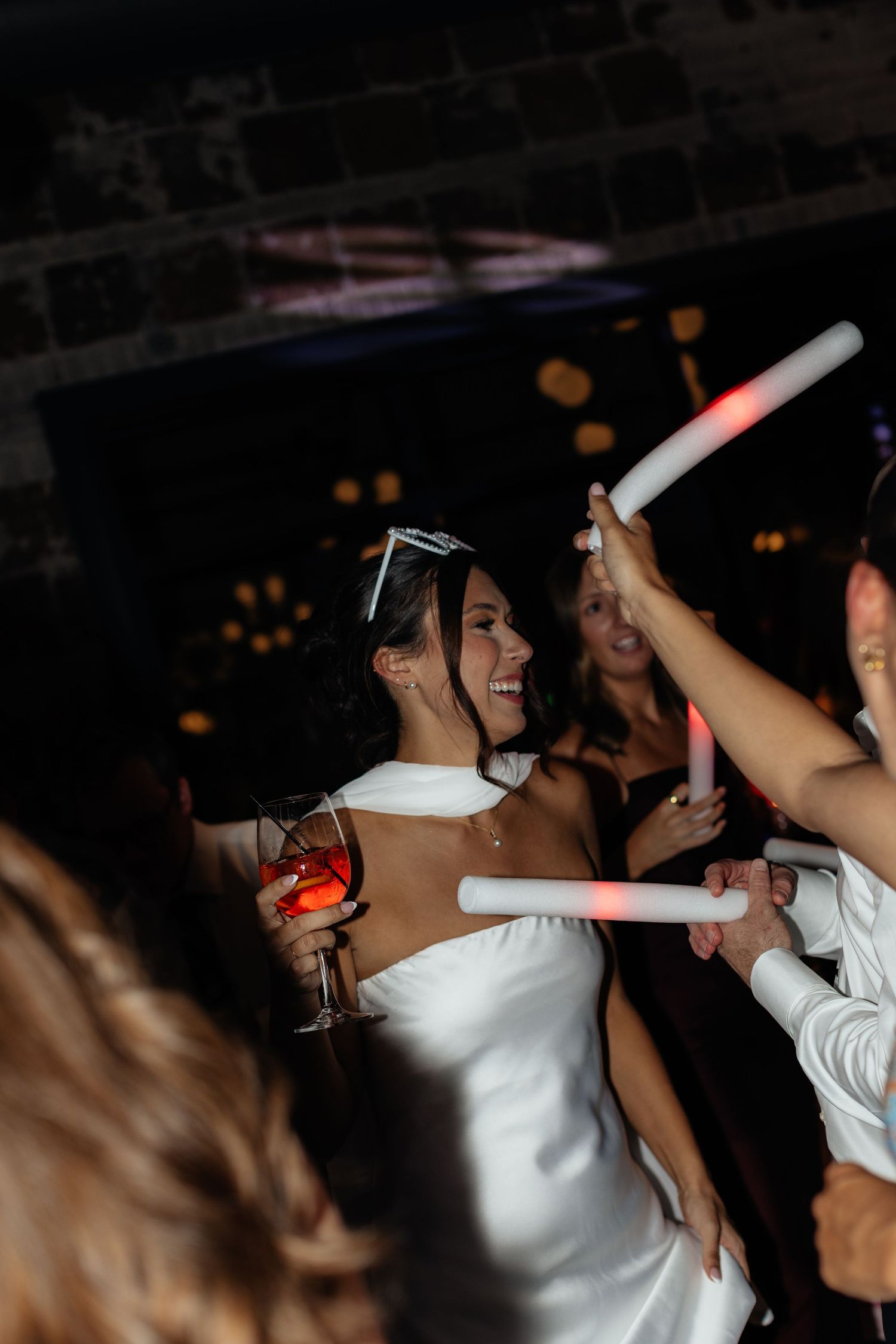 Wedding guests dancing and having fun in a dimly lit reception venue.