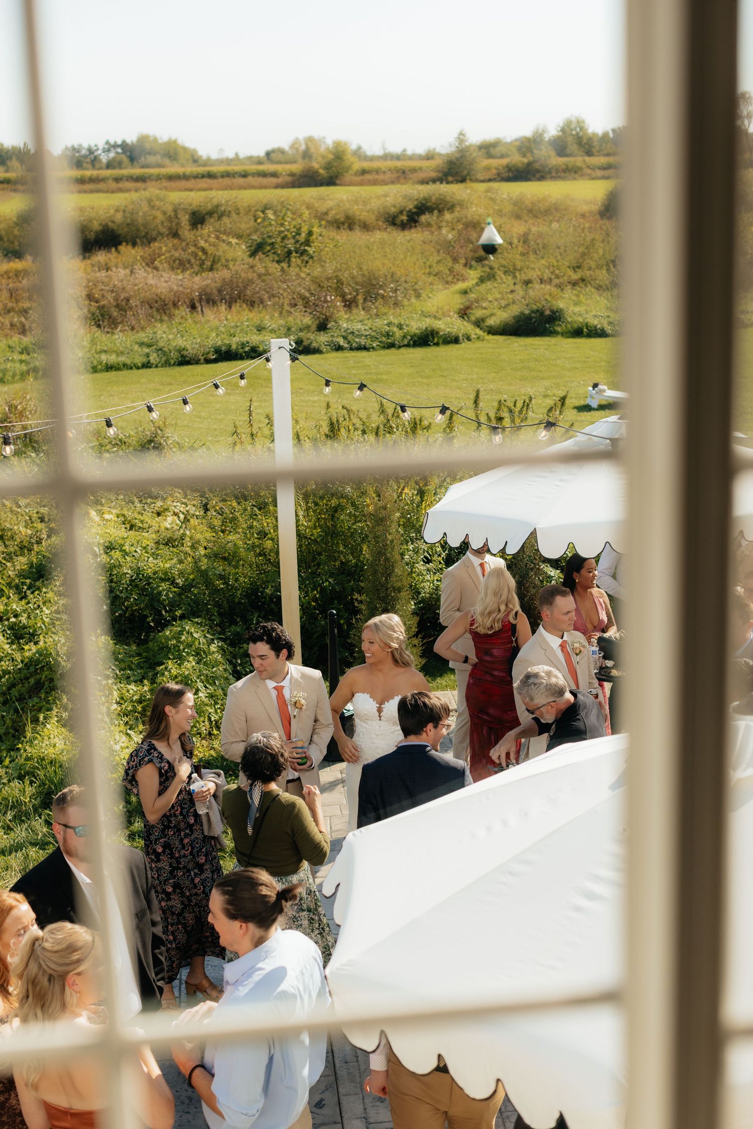 Wedding reception guests mingle under a white tent in an outdoor garden setting.
