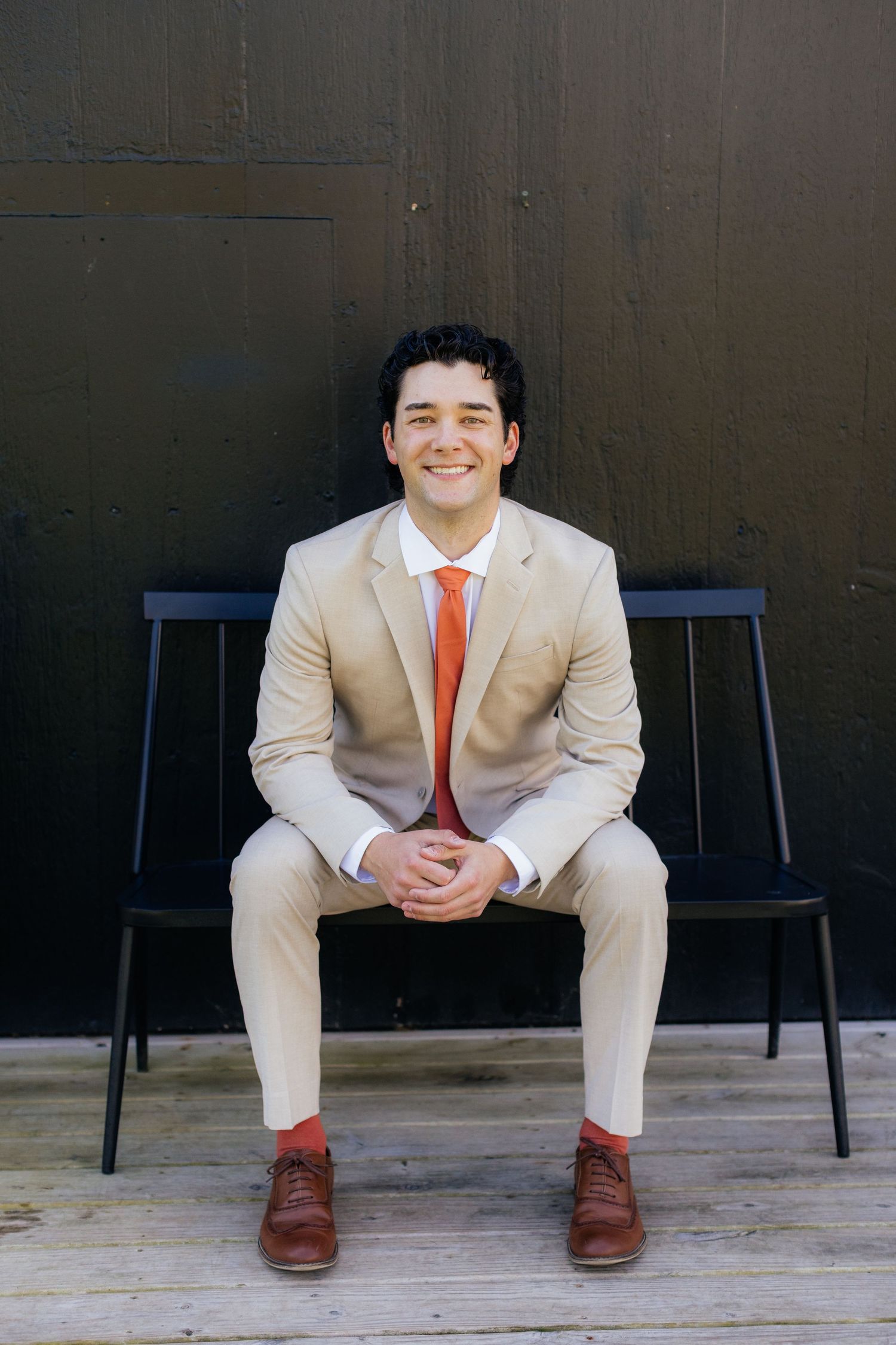 Person wearing beige suit with orange tie sits on wooden bench in artistic portrait series.