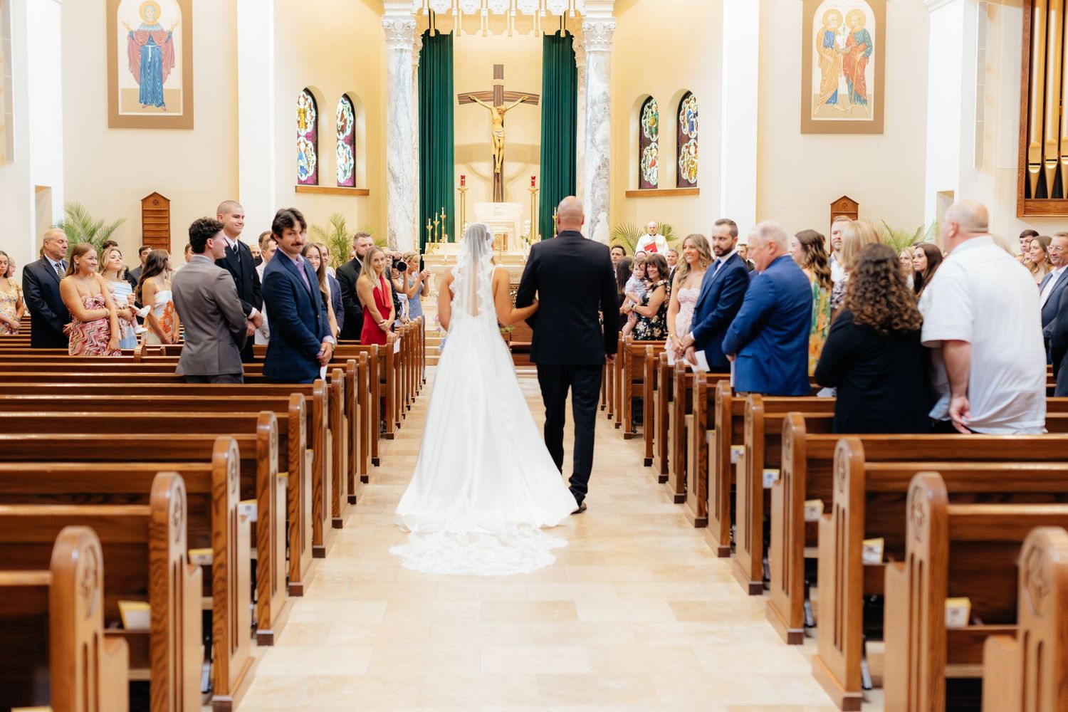 Wedding ceremony in progress inside a traditional Catholic church with guests seated in pews.