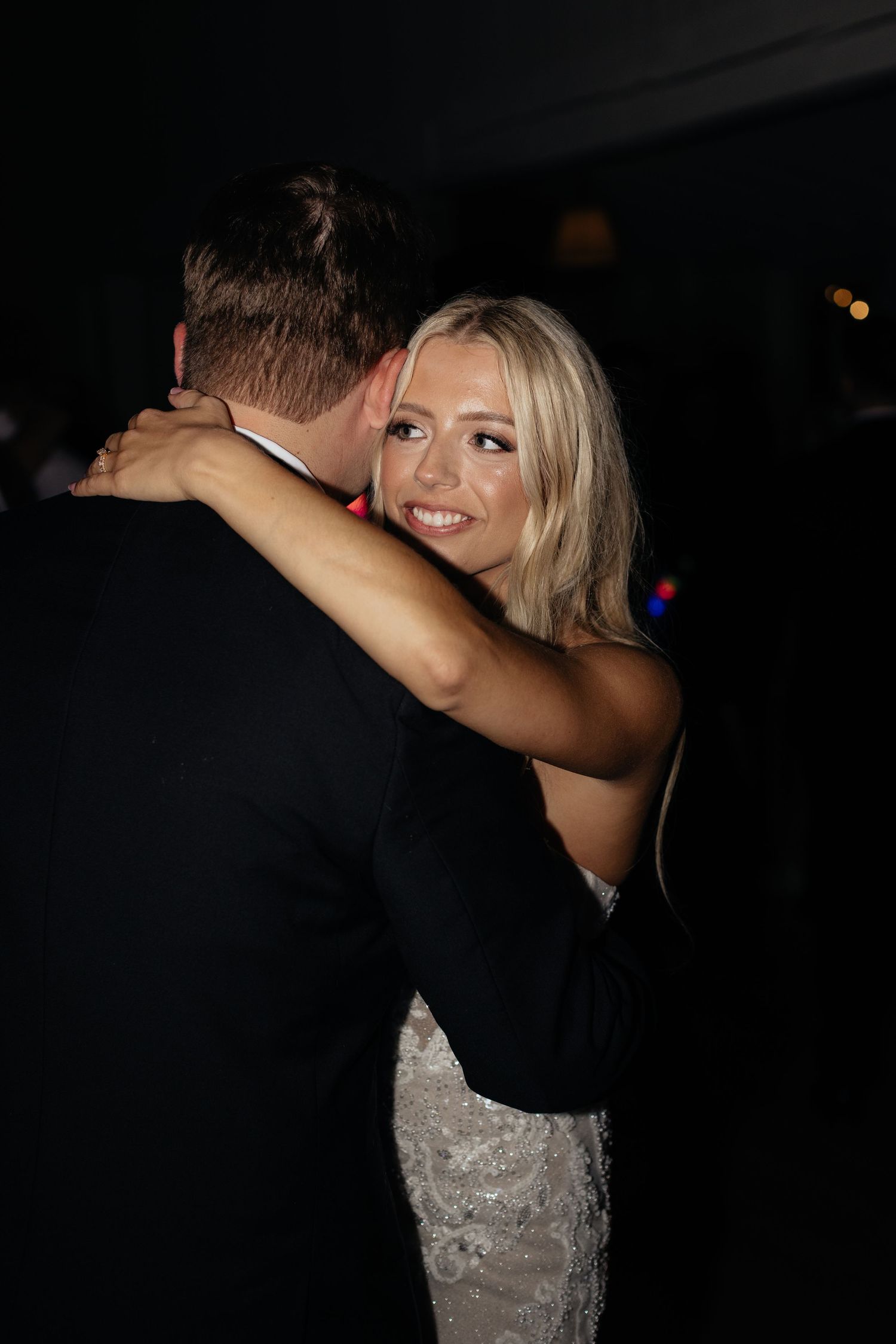Couple dancing in an intimate moment at a wedding reception with dramatic lighting.