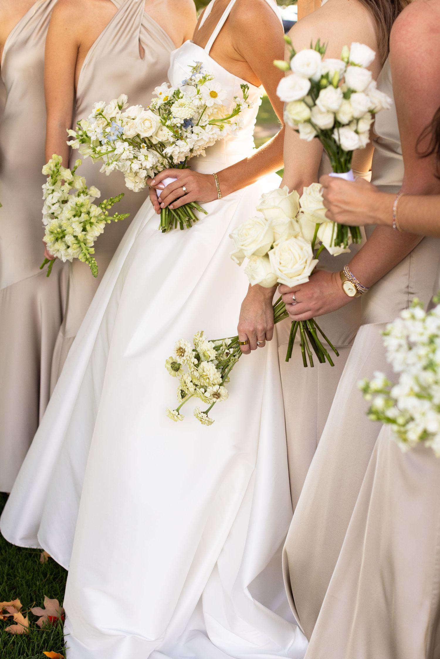Wedding party holds white and green floral bouquets against neutral colored dresses.