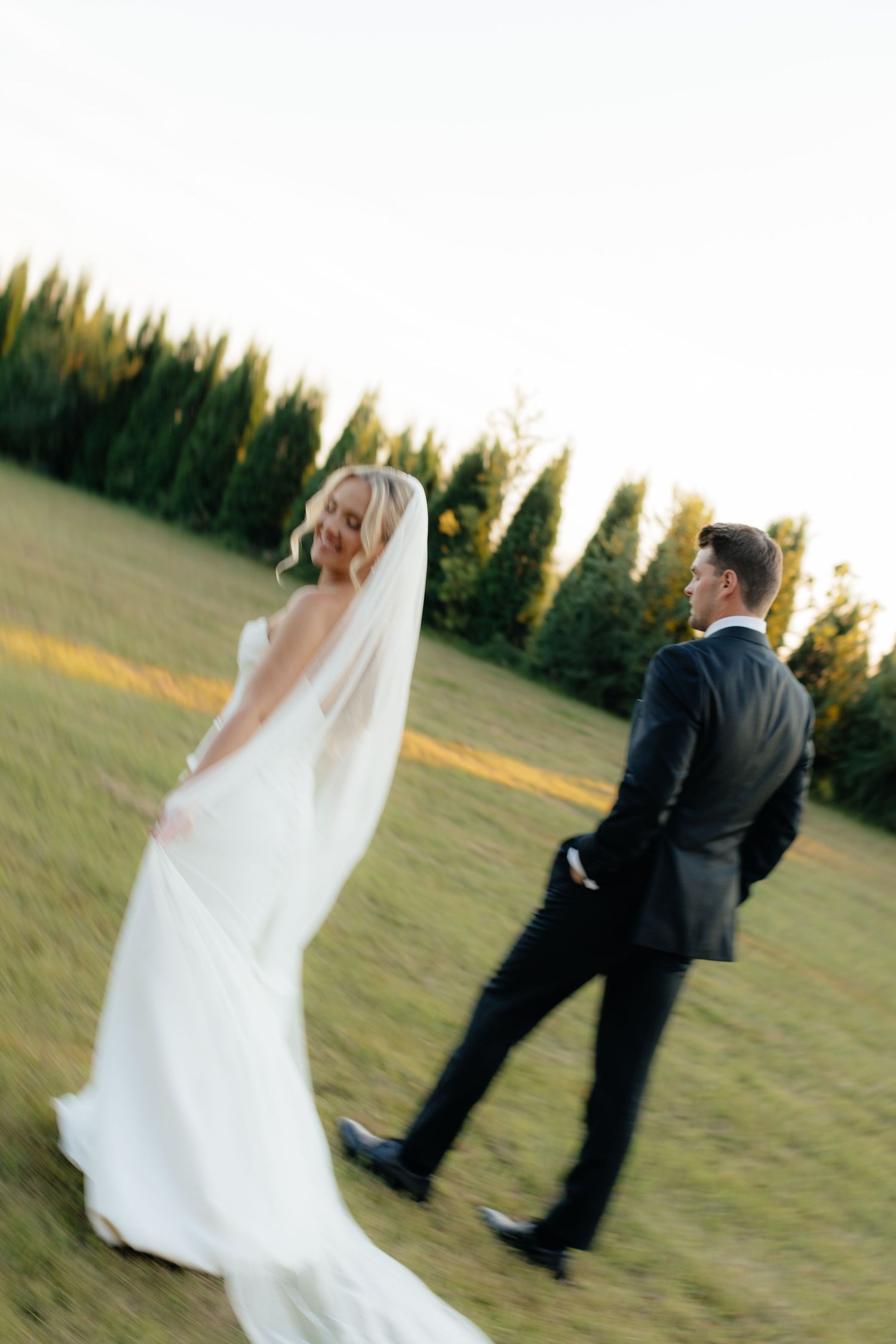 Wedding couple walks away from camera with motion blur effect at sunset.