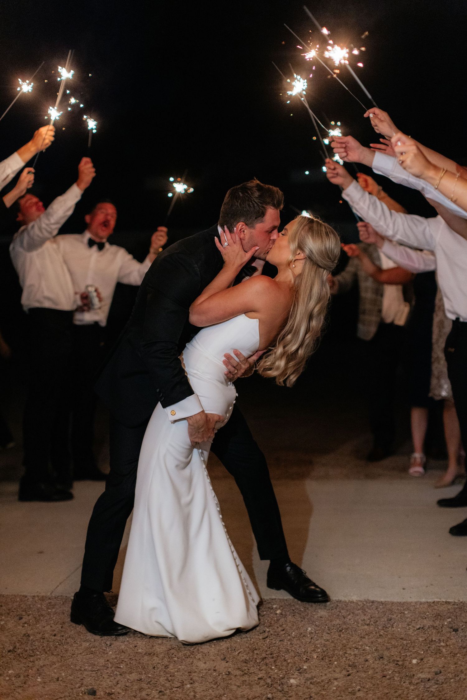 Newlyweds dance together under sparklers at their wedding reception during a romantic nighttime celebration.