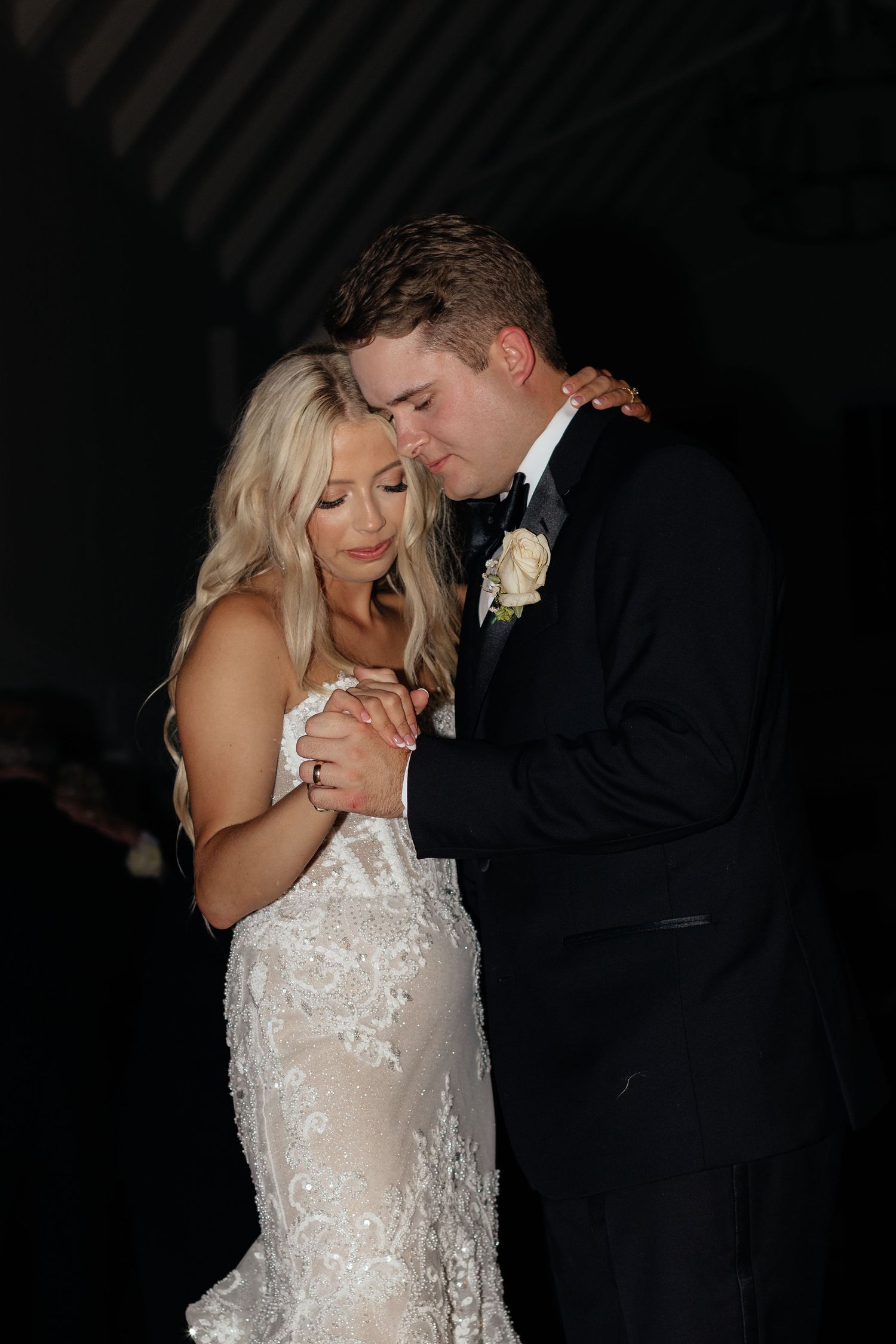 Romantic first dance between newlyweds, bride in white lace gown and groom in black tuxedo.