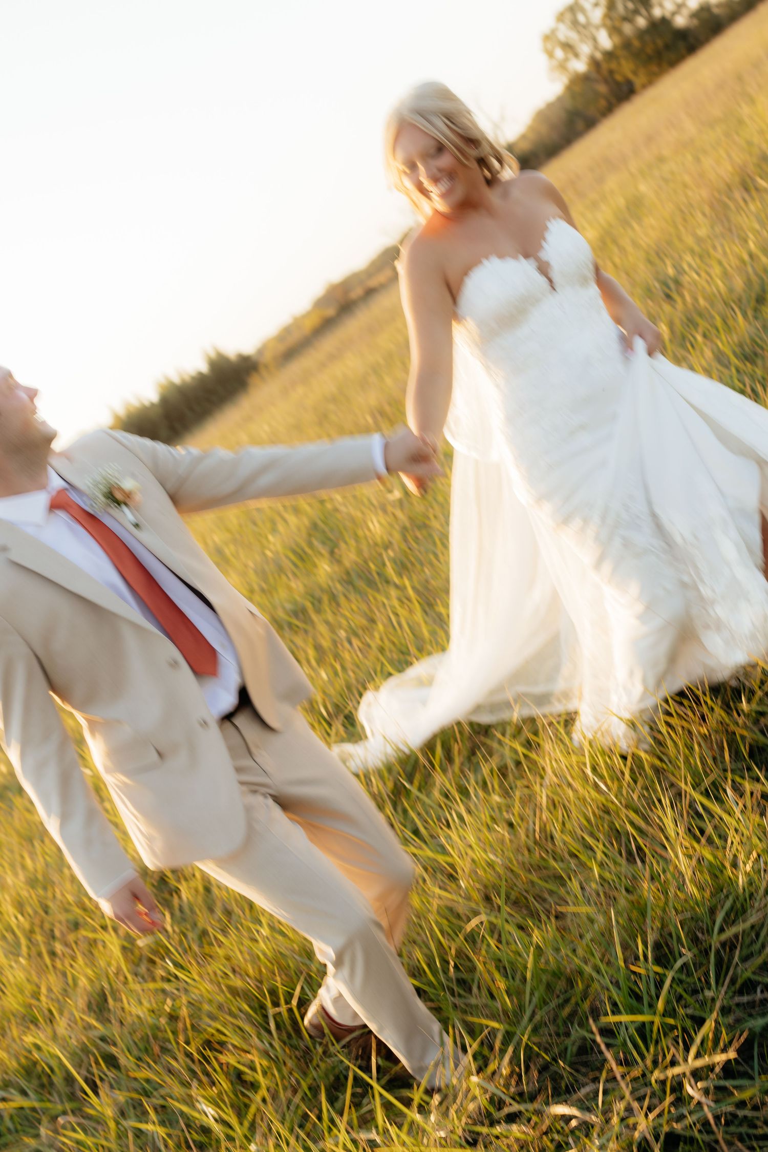 Wedding couple dancing and twirling in a sun-drenched field.