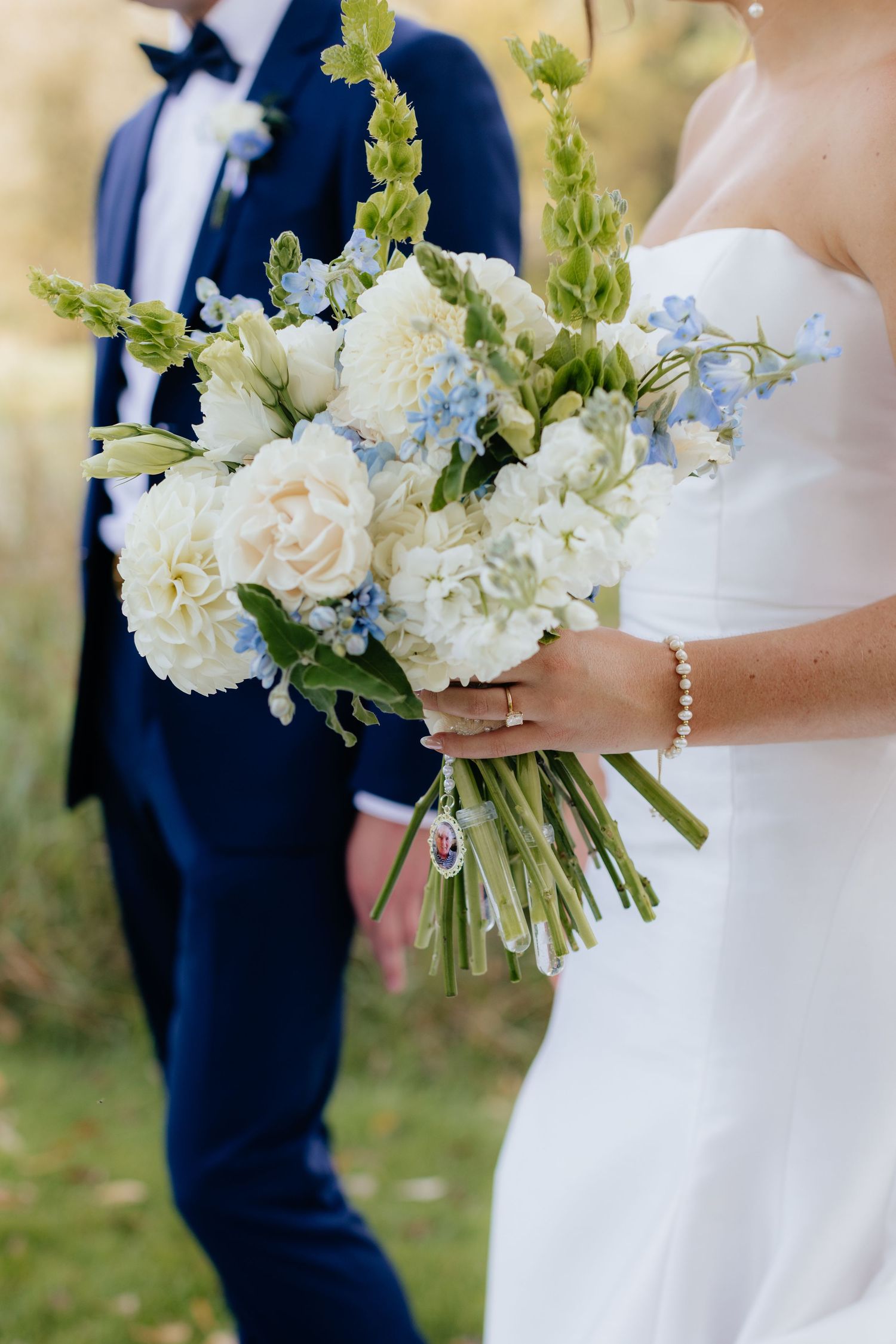 A white and blue wedding bouquet with delicate flowers against a bridal gown.