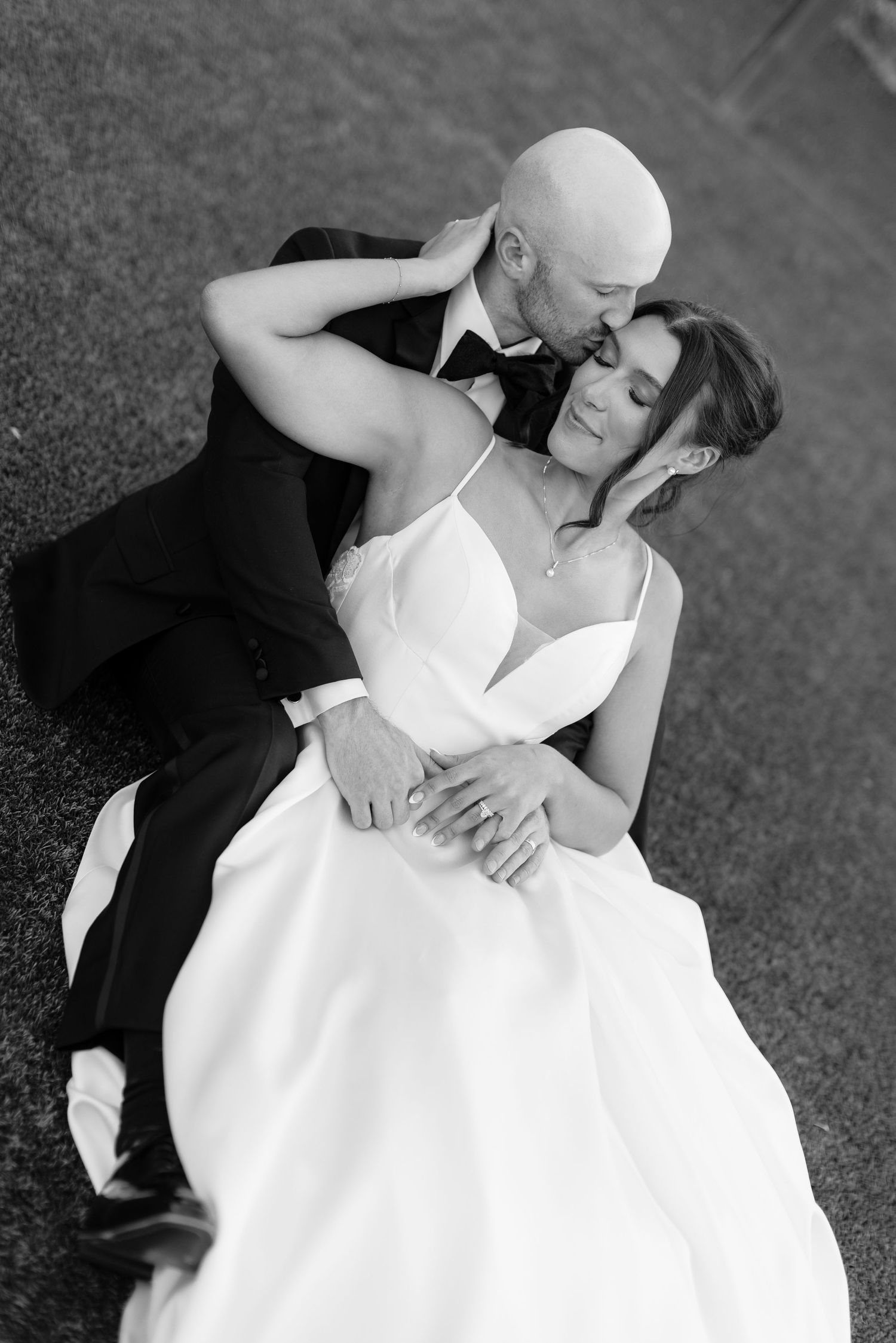 Black and white portrait of newlyweds embracing on grass during wedding celebration.