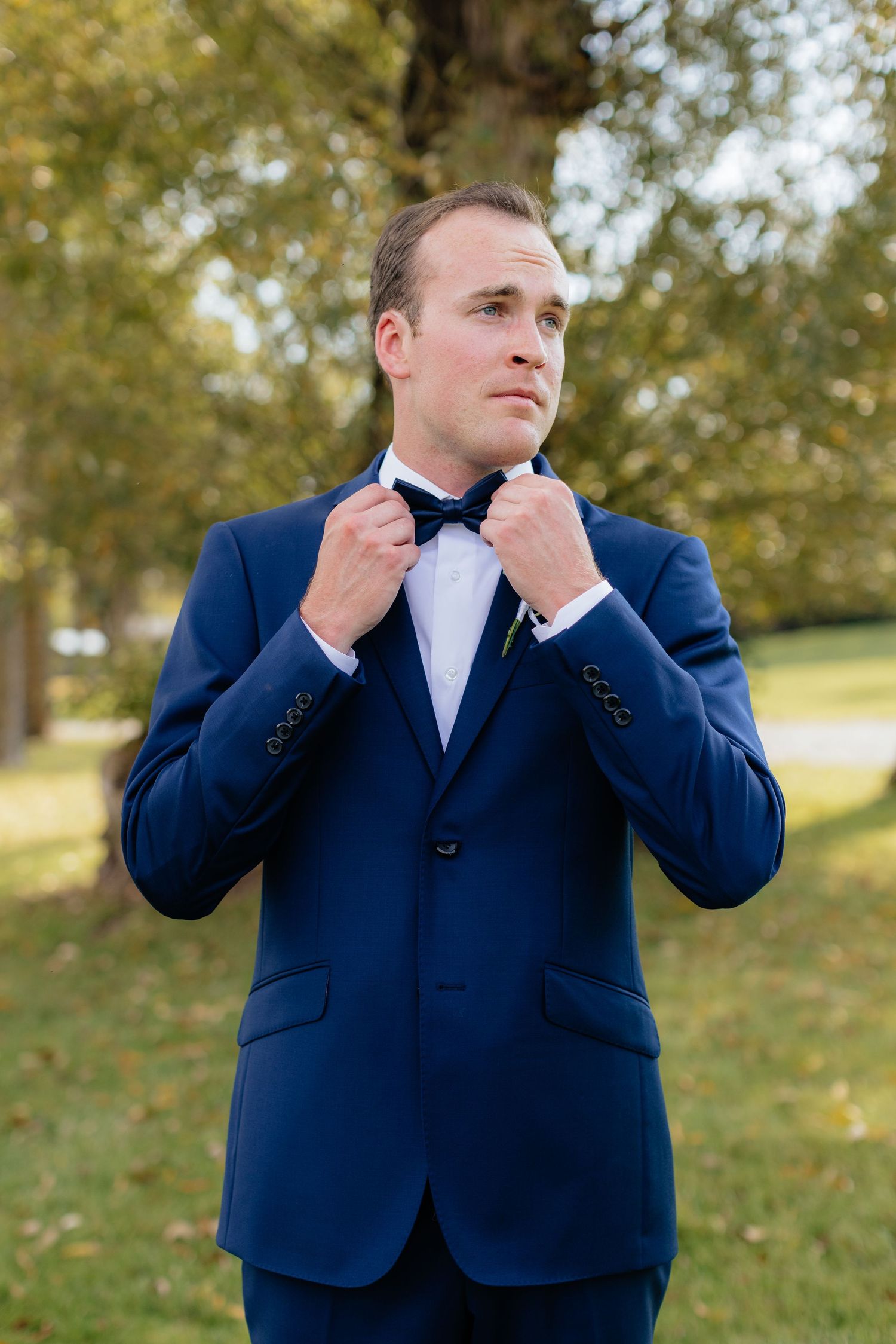 Groom in dark blue tuxedo adjusts his bowtie before the ceremony.