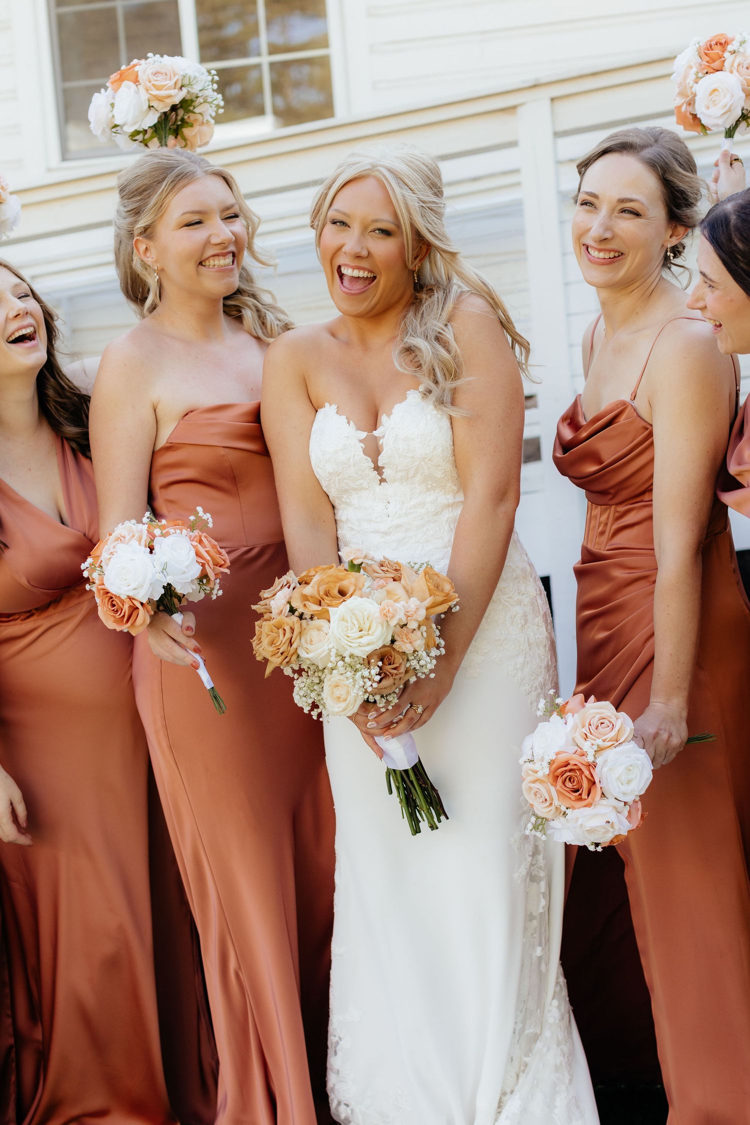 Wedding party in rust-colored bridesmaid dresses posing together with bouquets.
