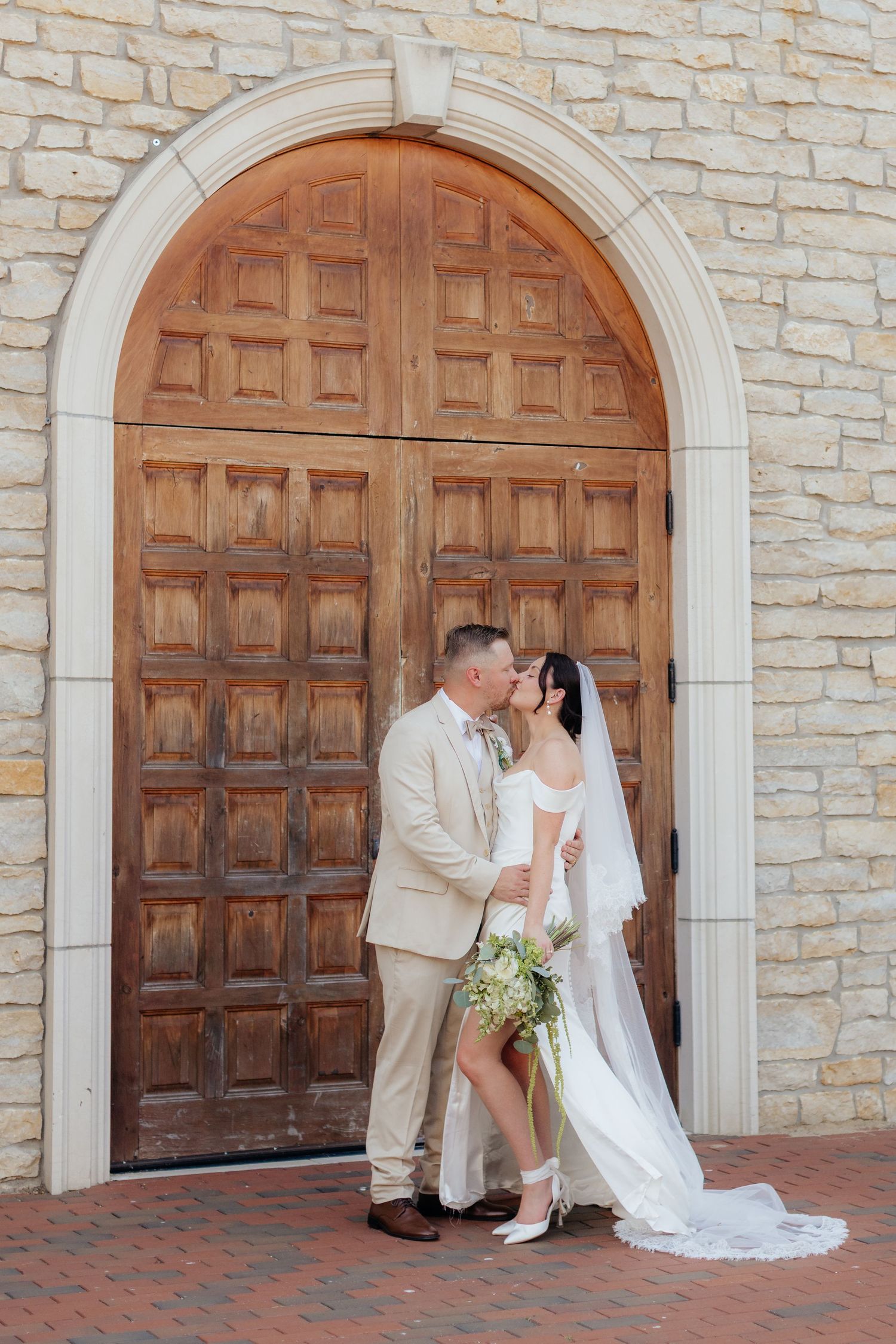 Romantic wedding scene against stone wall with wooden arched doors as backdrop.