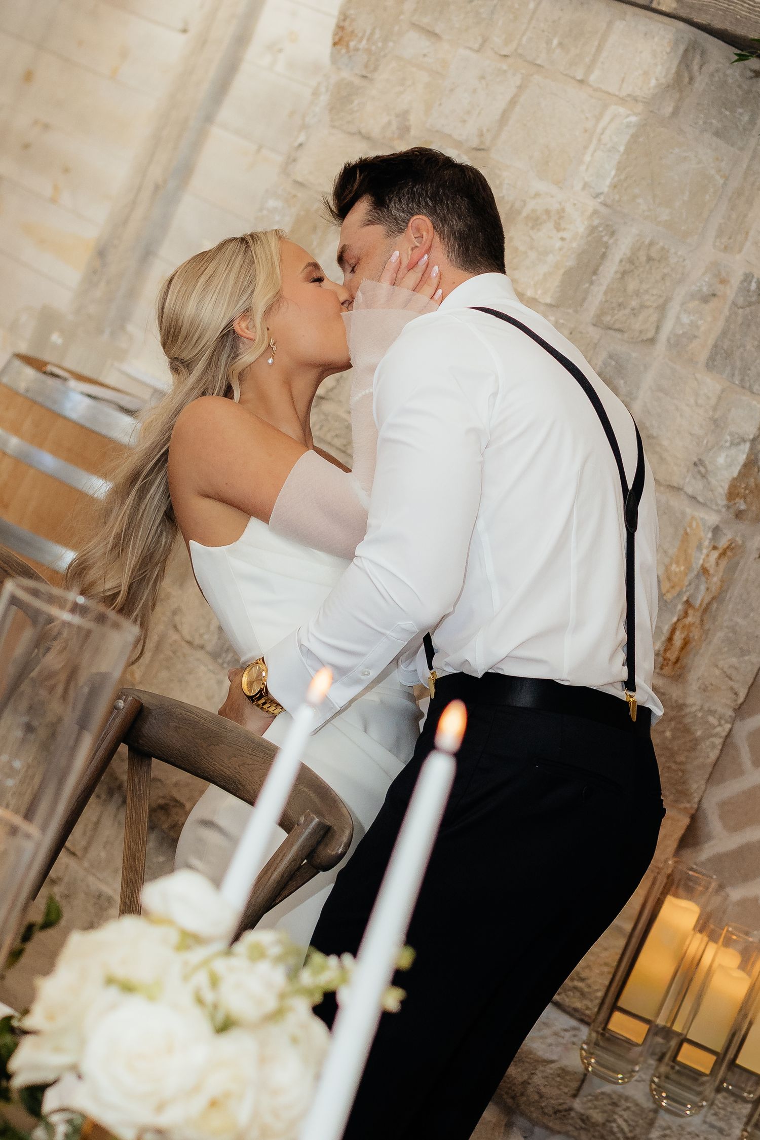 An intimate moment between newlyweds near candlelit tables with stone walls in the background.