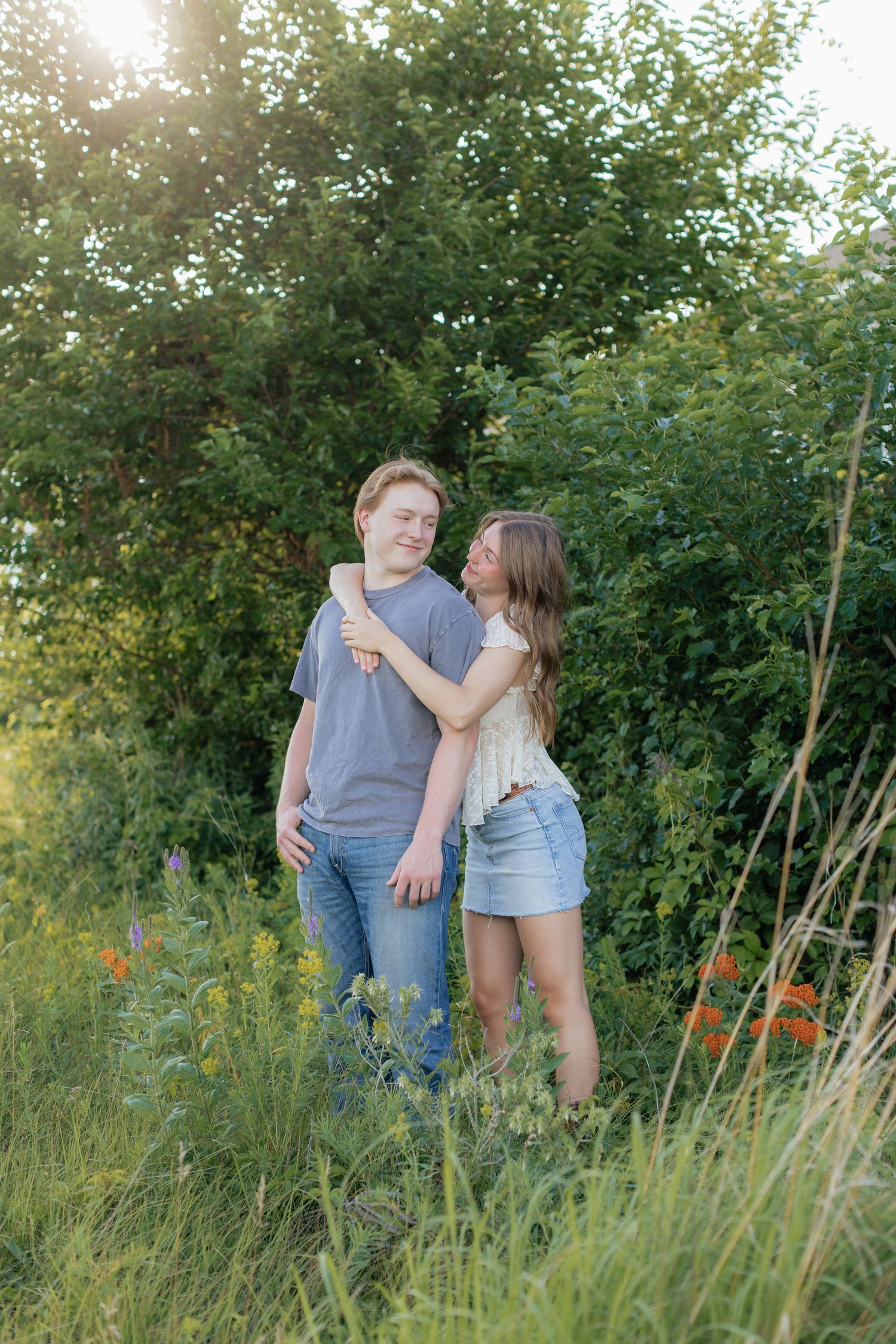 Couple shares intimate moment in tall summer grass during sunset photoshoot.
