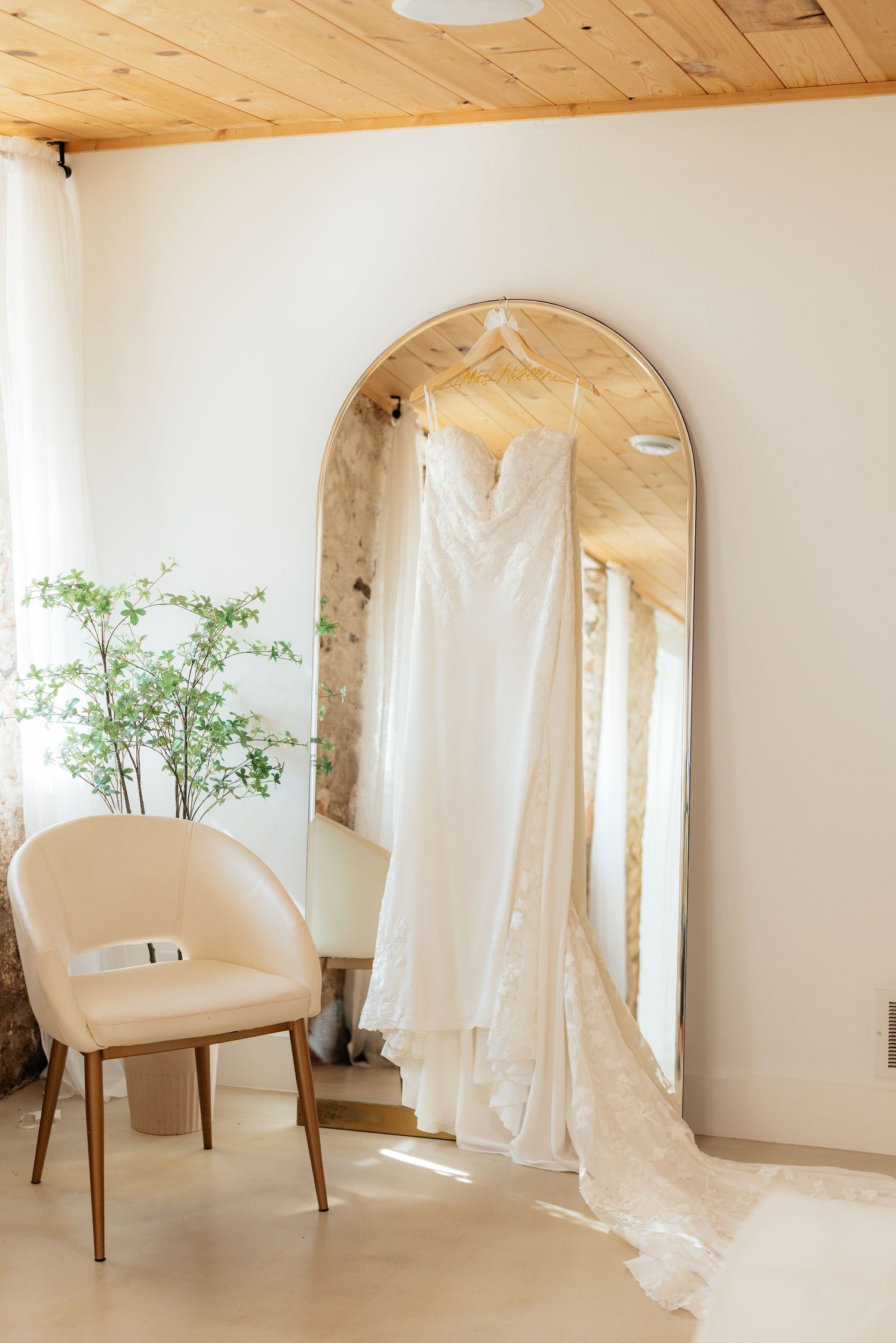 A bridal preparation room with arched mirrors, white chair, and hanging wedding dress.