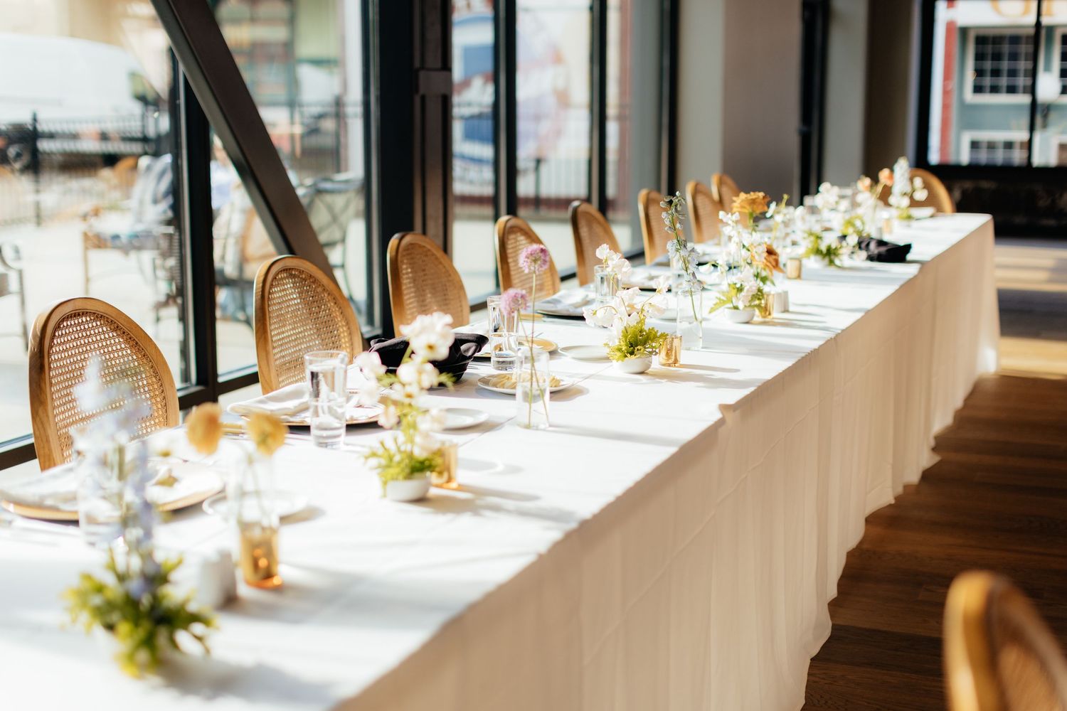 Long banquet table set for a wedding reception with elegant place settings and natural light.