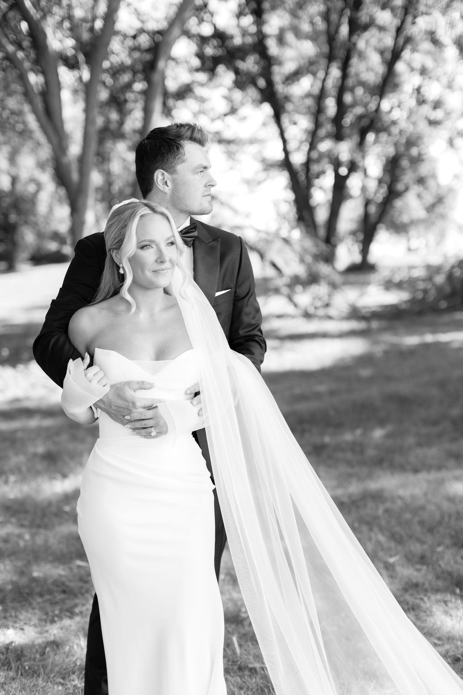 Black and white portrait of couple with flowing veil in natural outdoor setting.