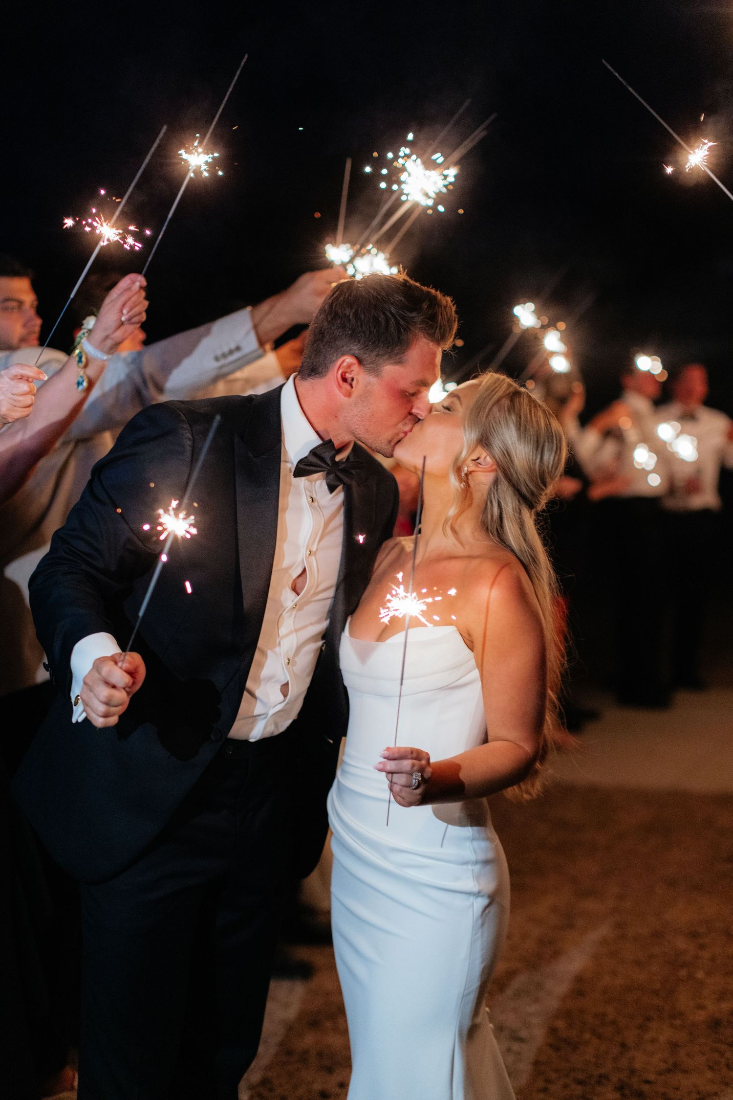 Romantic sparkler exit moment with couple sharing a kiss surrounded by glowing lights.